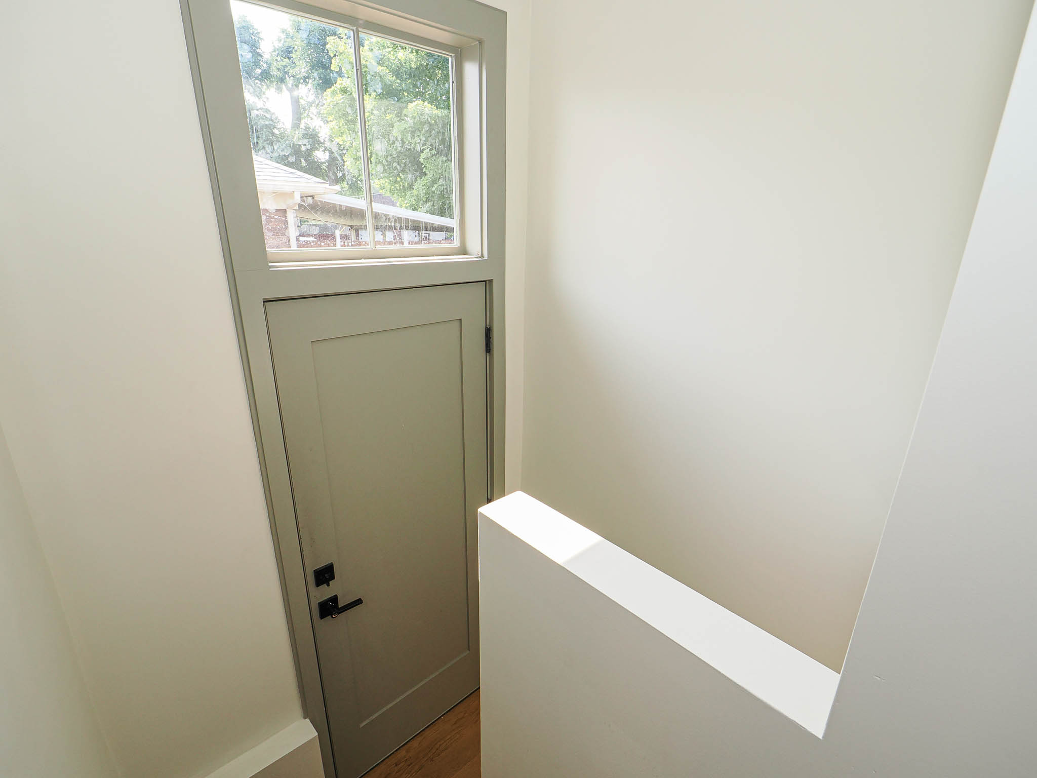 Interior doorway with transom window, featuring a paneled door, black hardware, and light wood-finish flooring