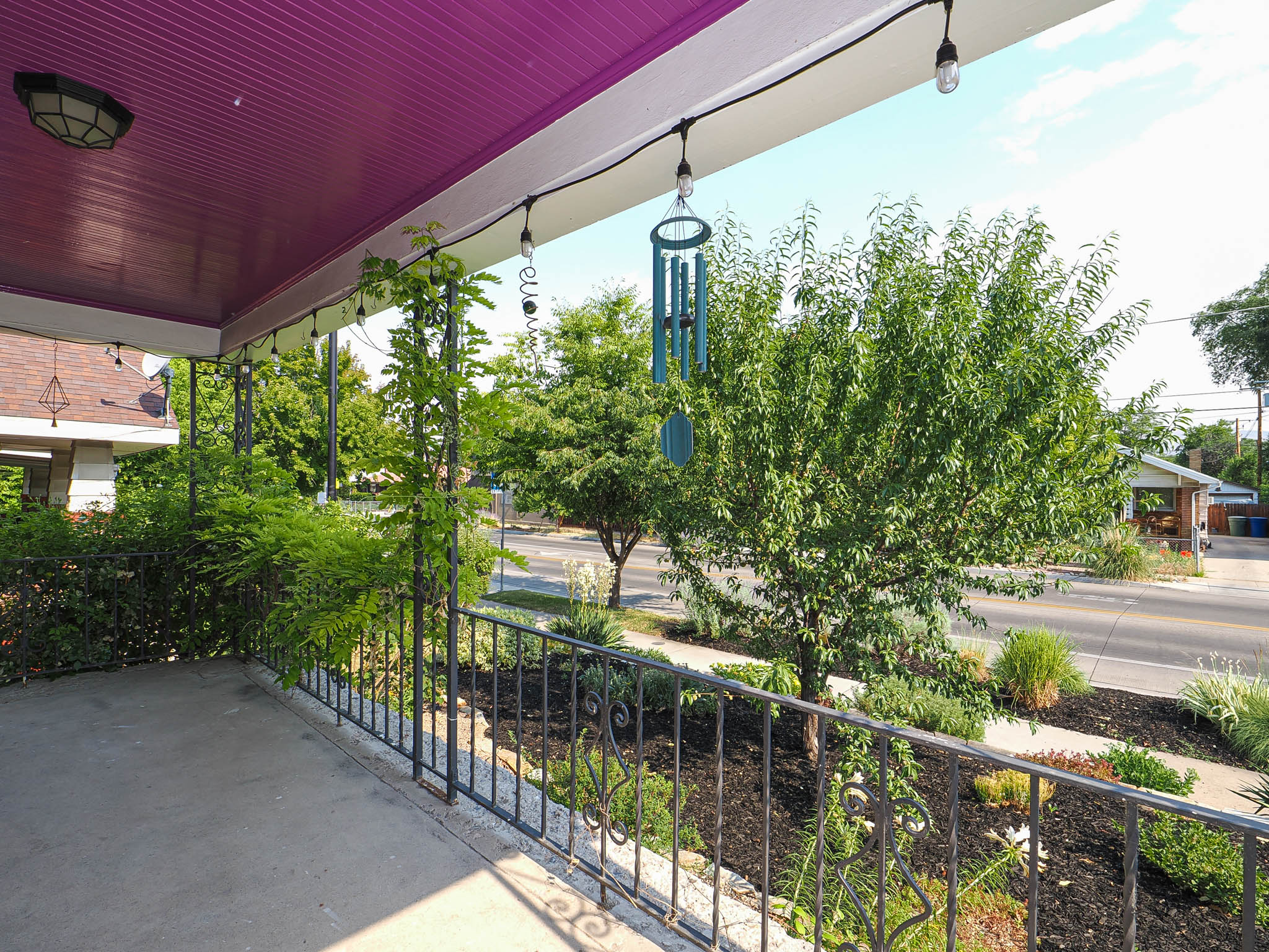 Covered porch featuring a vibrant purple ceiling, concrete flooring, and decorative wrought iron railing