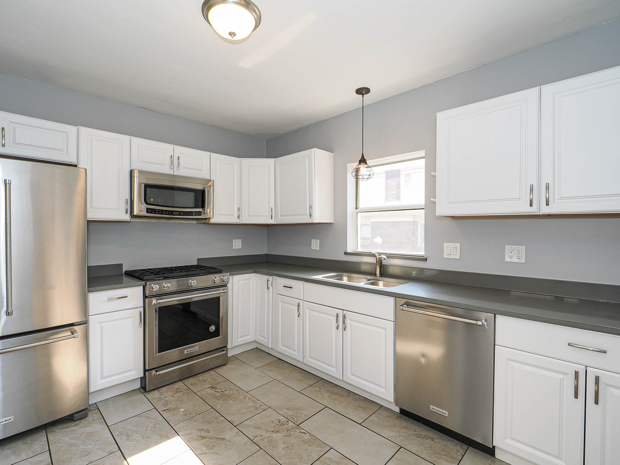 Kitchen featuring white shaker cabinetry, stainless steel appliances, dark countertops, and neutral-toned tile flooring