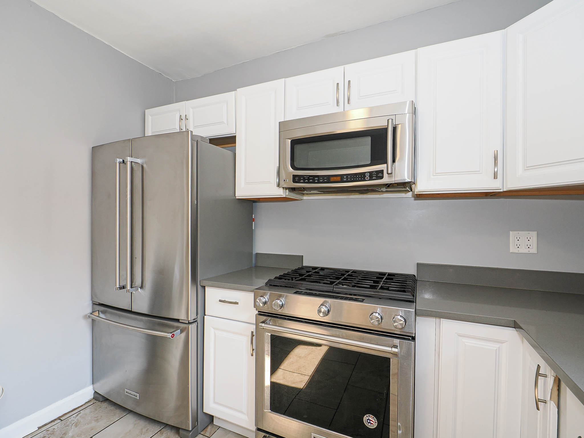 Kitchen featuring white cabinetry, gray countertops, stainless steel appliances, and wood-finish flooring