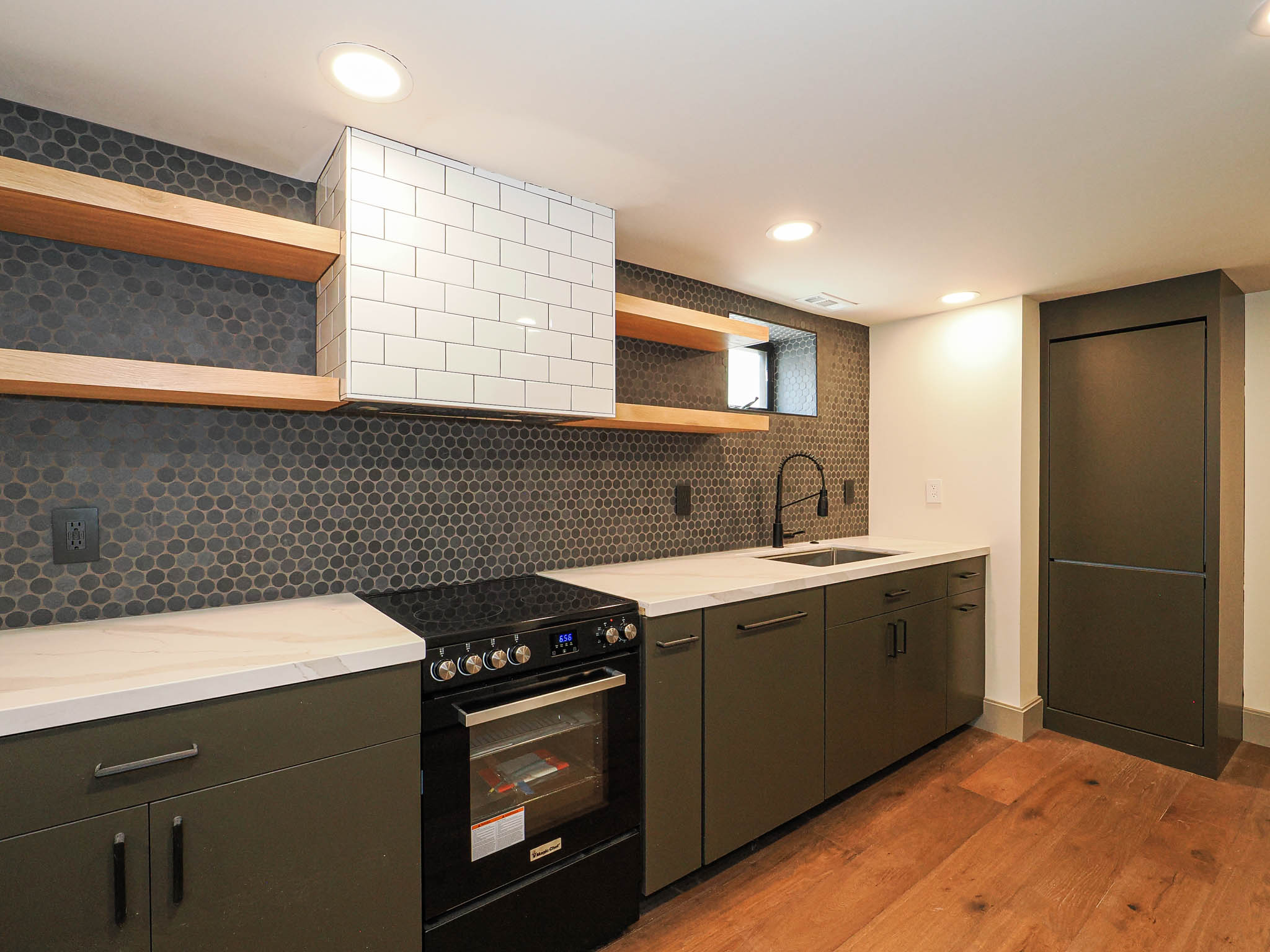 Kitchenette featuring a black appliance suite, dark green cabinetry, white countertops, and a full-height dark penny tile backsplash