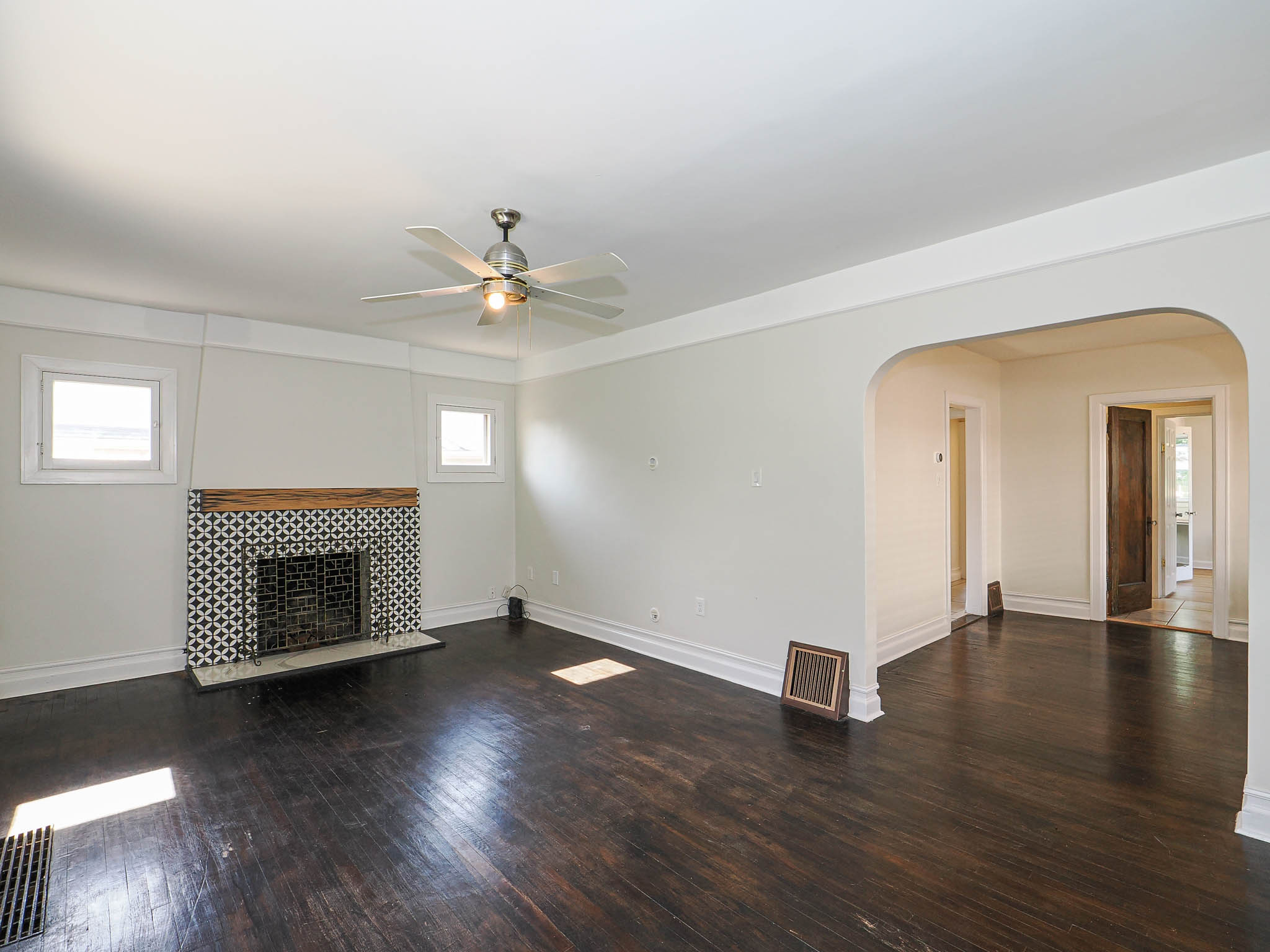 Living room featuring dark wood-finish flooring, a patterned tile fireplace surround with a wood mantel, and a ceiling fan with integrated lighting