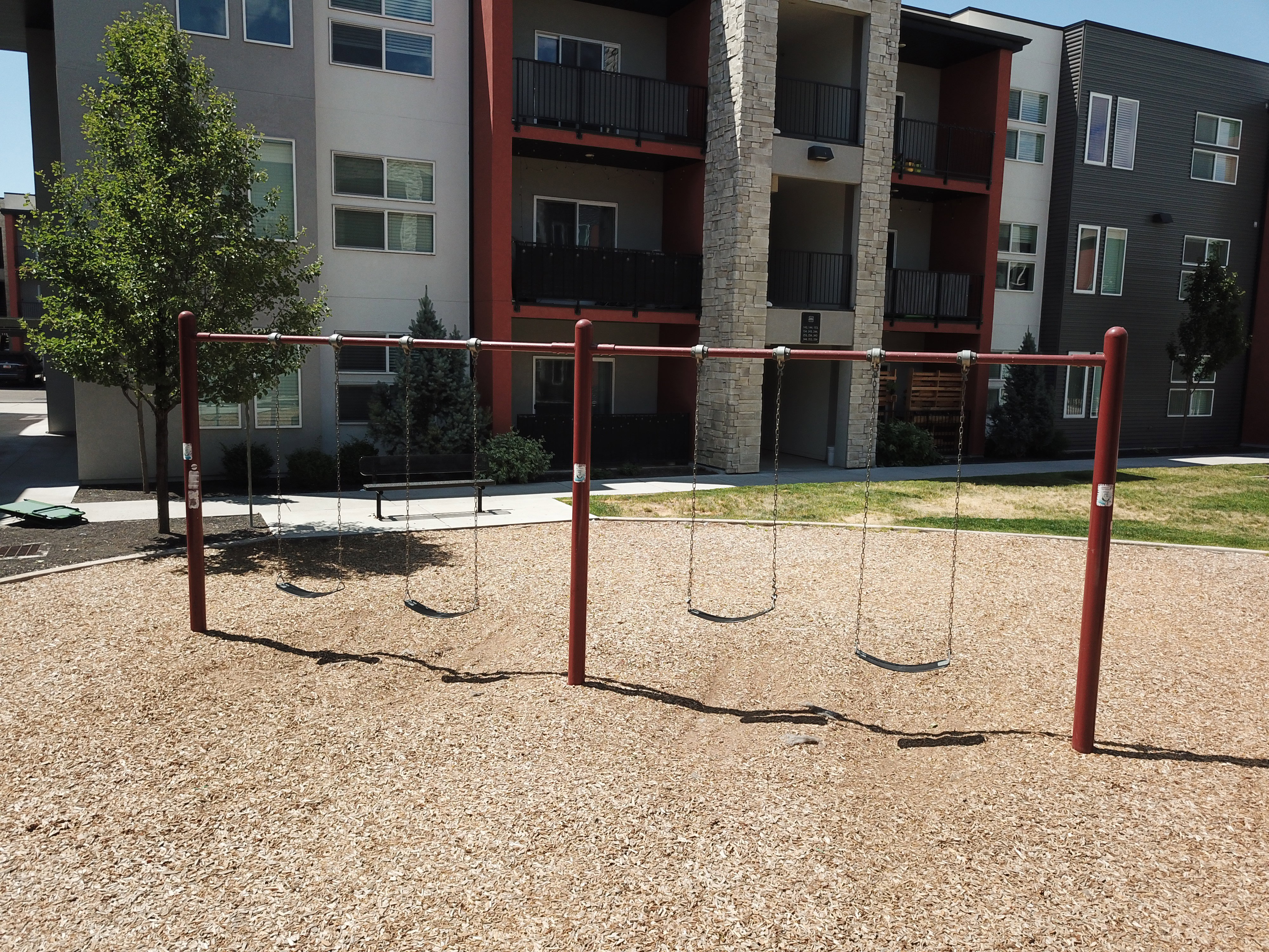 Outdoor play area featuring a swing set with four swings, set over wood chip surfacing