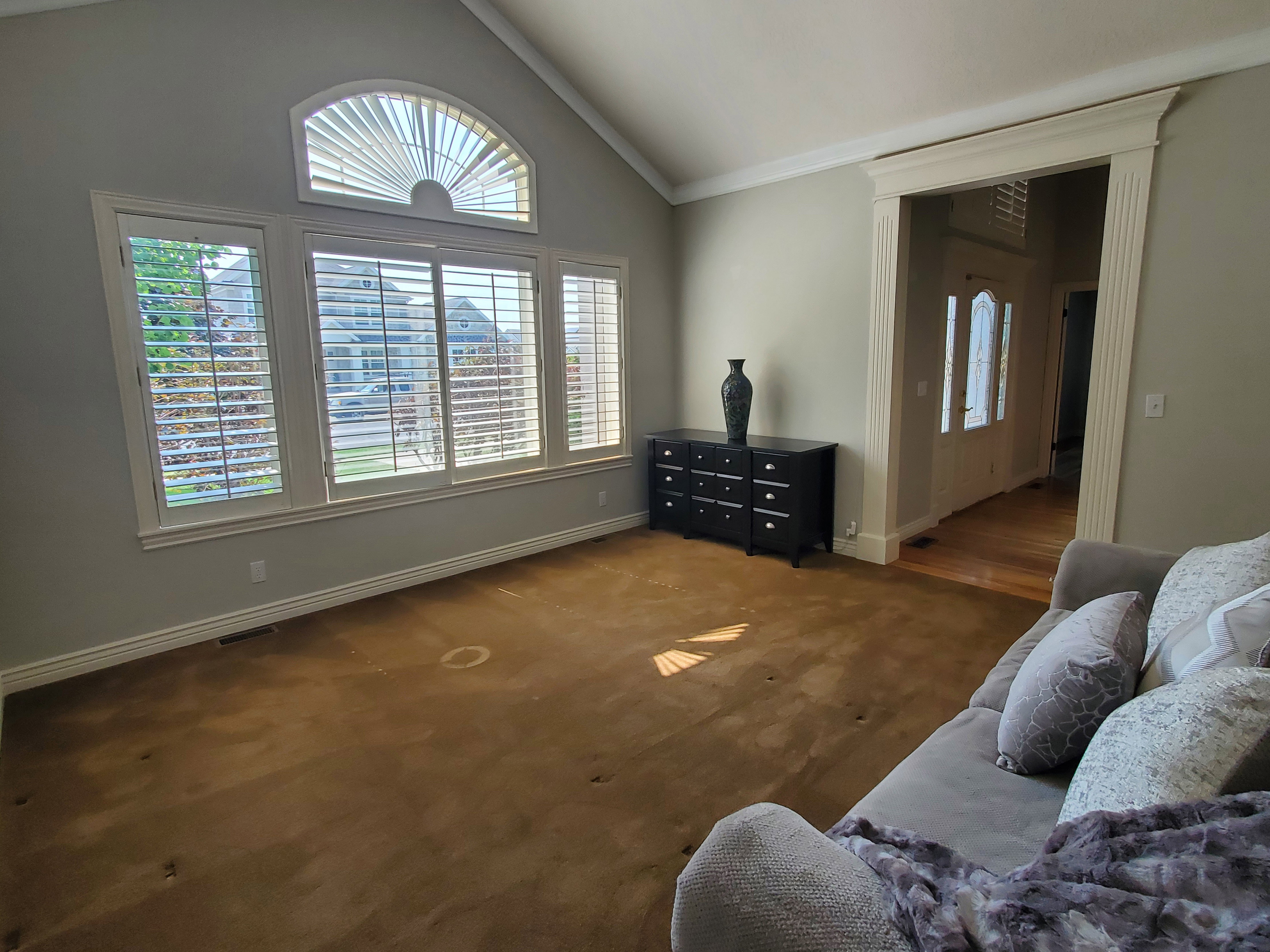Spacious living area featuring vaulted ceilings, crown molding, and extensive window treatments including an arched transom window