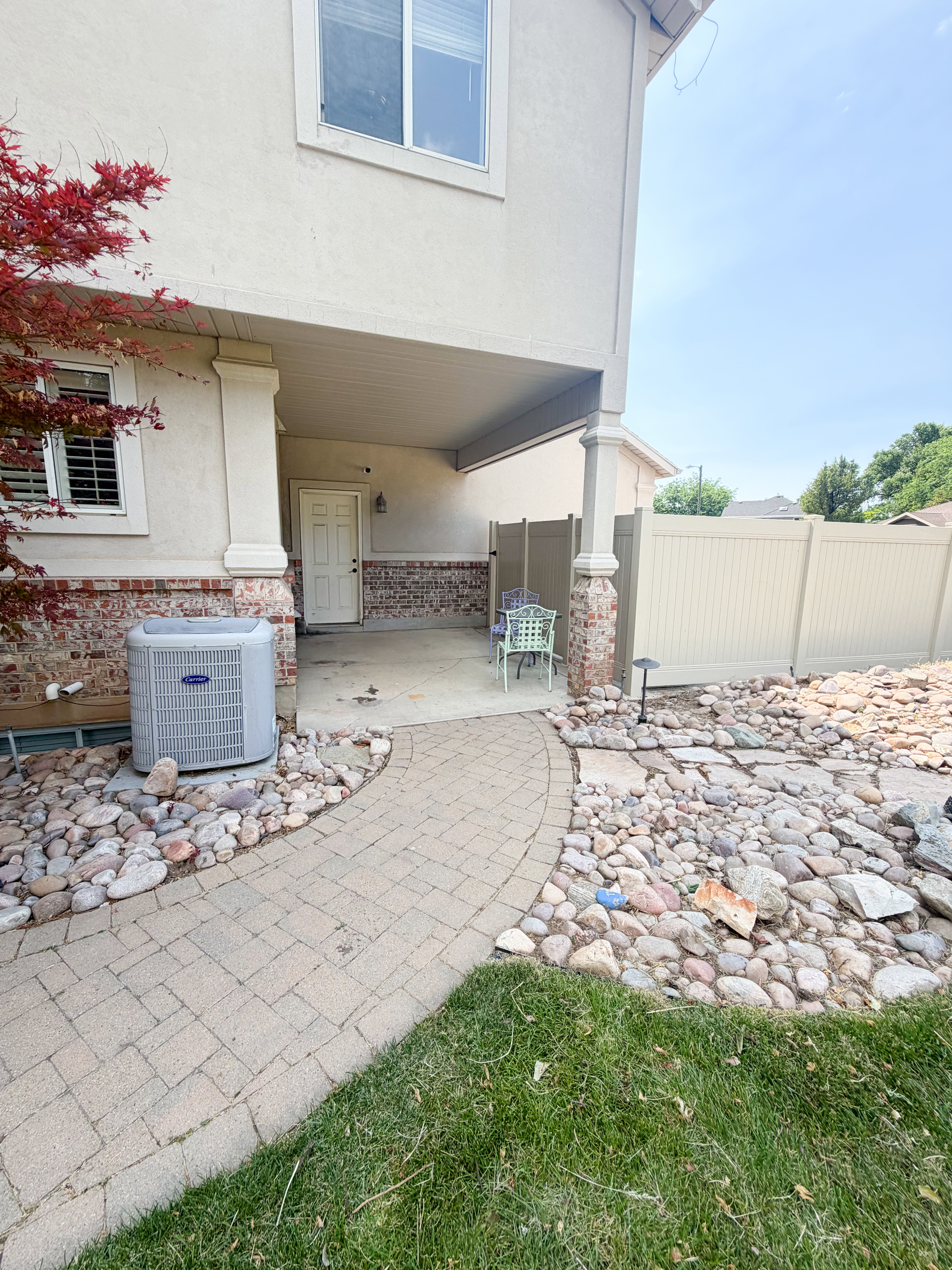 Covered patio with a paver walkway, stucco exterior, brick accents, and a privacy fence