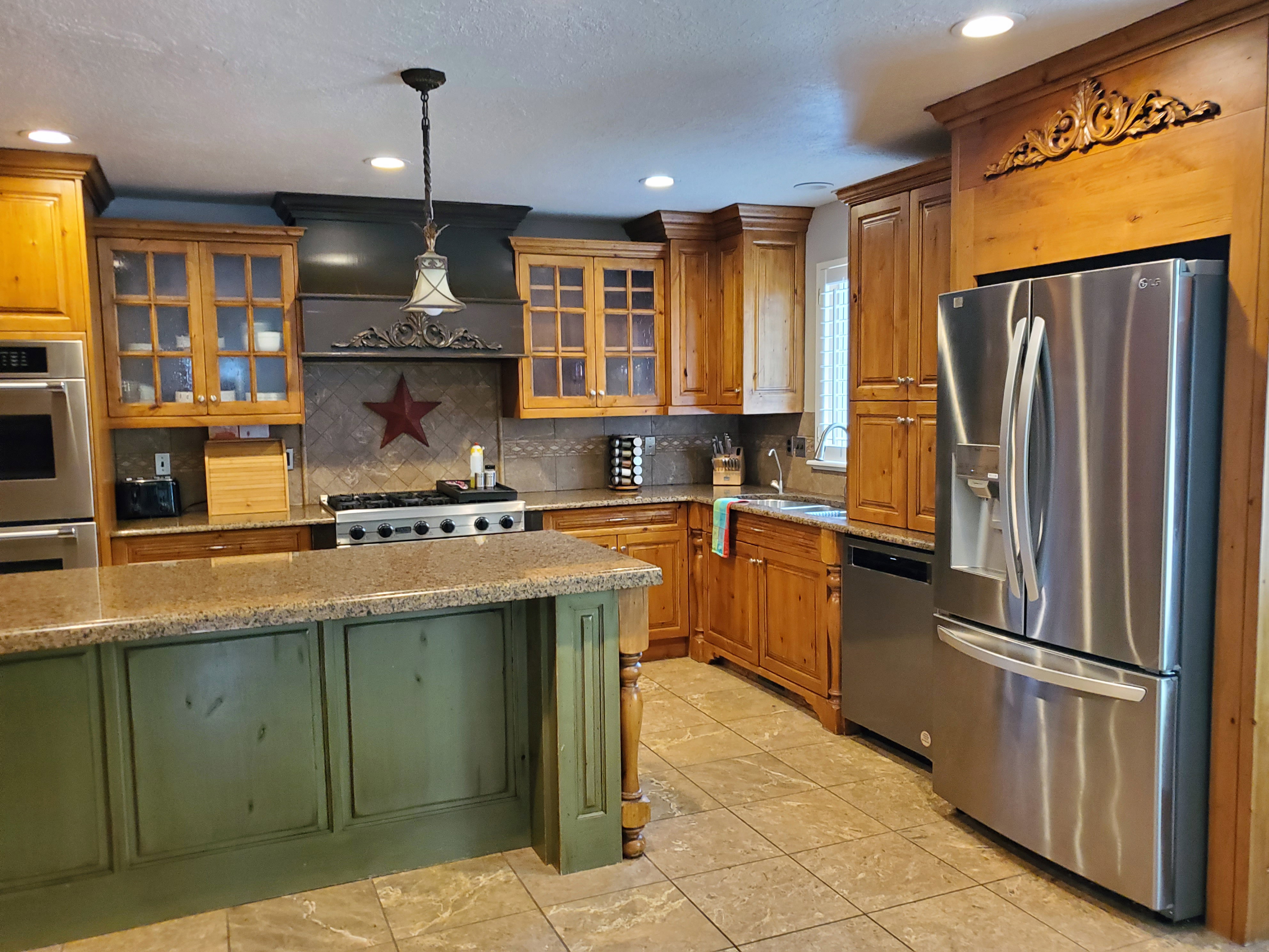 Kitchen featuring a central island with a distressed green finish, coordinating granite countertops, wood cabinetry with some glass-front doors, and stainless steel appliances