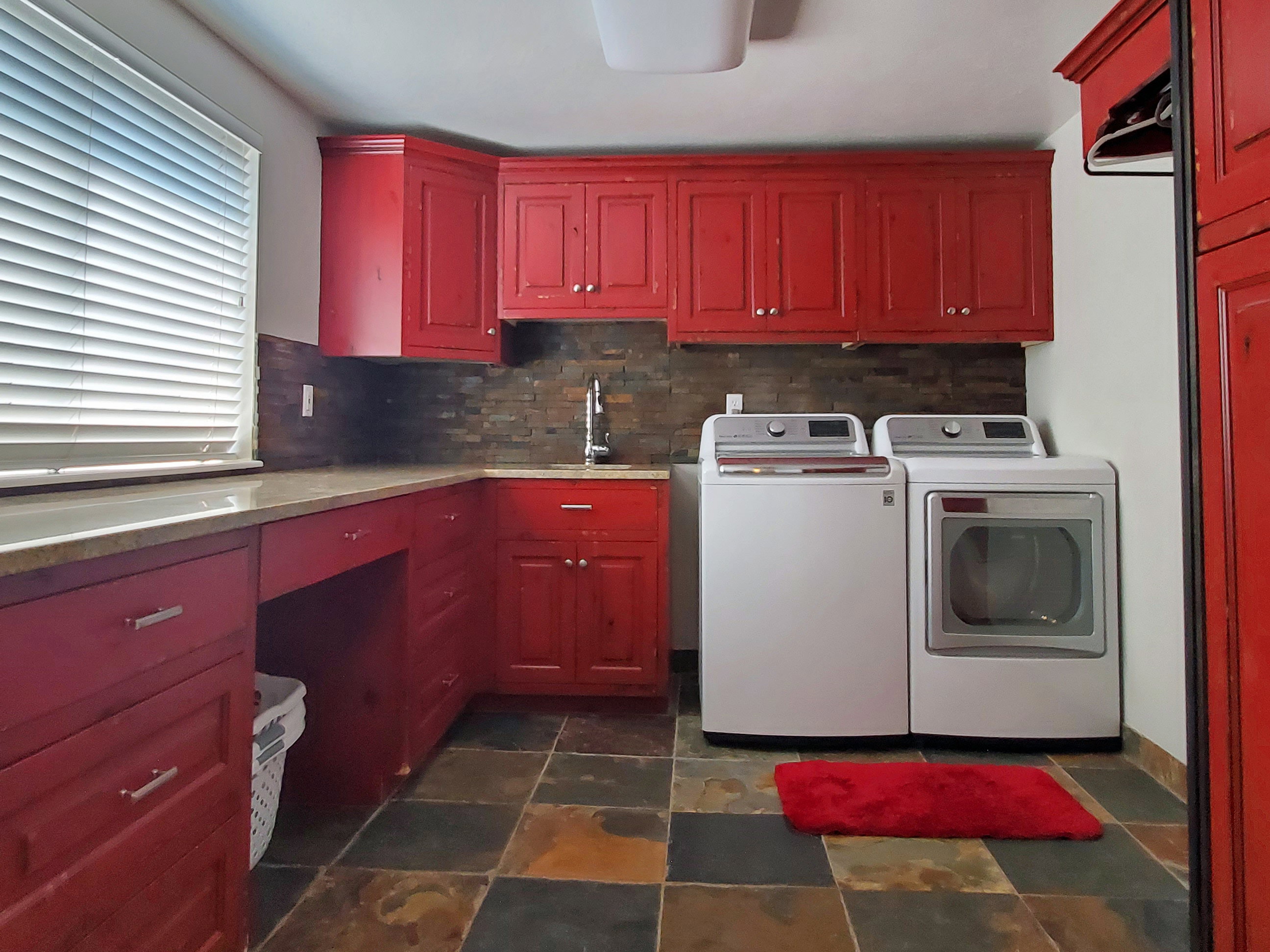 Laundry room featuring extensive red cabinetry, a granite-finish countertop, and a dark stone-finish backsplash