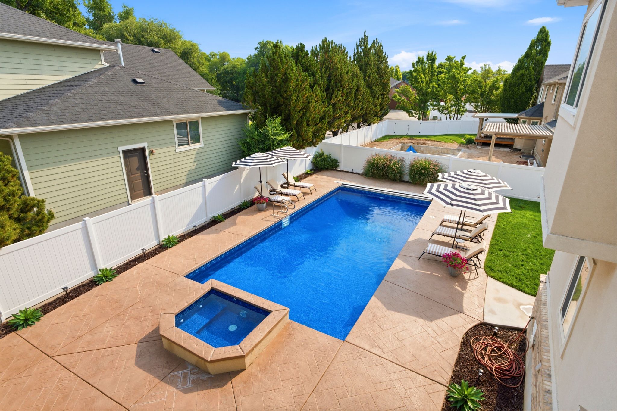 Expansive outdoor space featuring a rectangular swimming pool, integrated hot tub, and patterned stamped concrete patio