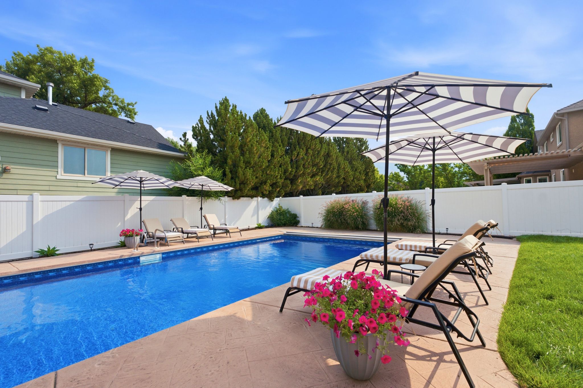 Rectangular swimming pool featuring a stamped concrete surround, white privacy fencing, and green landscaping