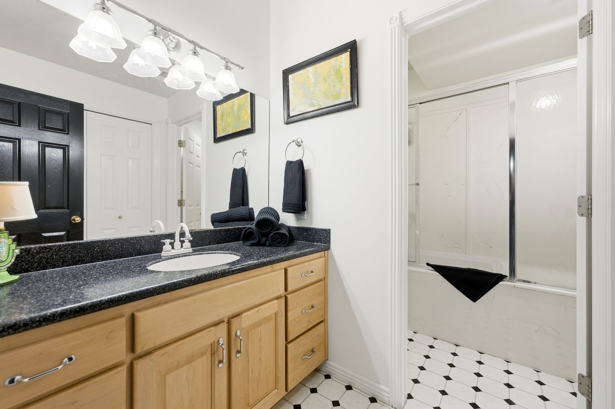 Bathroom vanity with a dark speckled countertop, light wood cabinetry, and an integrated white sink