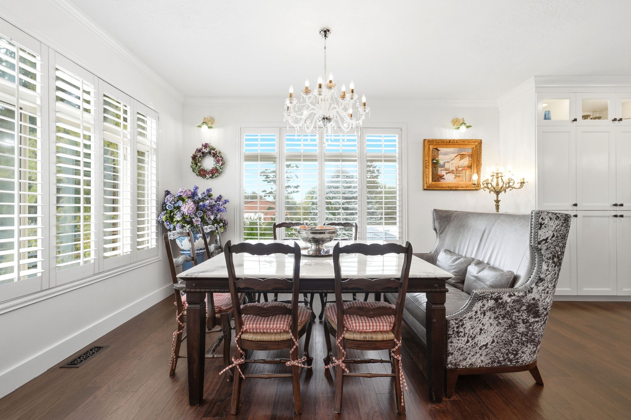 Dining area featuring wood-finish flooring, white plantation shutters, and a chandelier