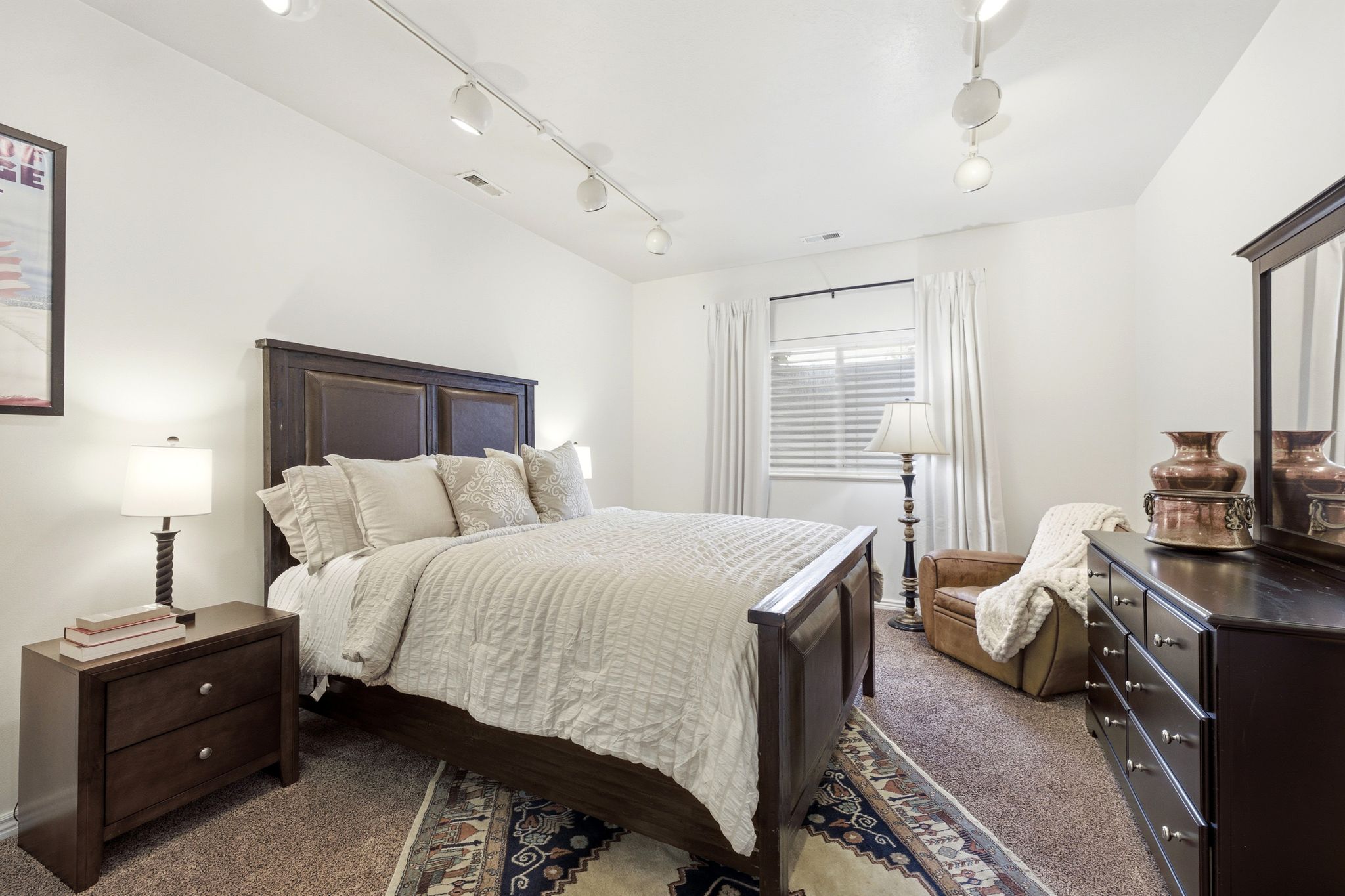 Spacious room featuring white walls, track lighting, and a window with blinds and curtains