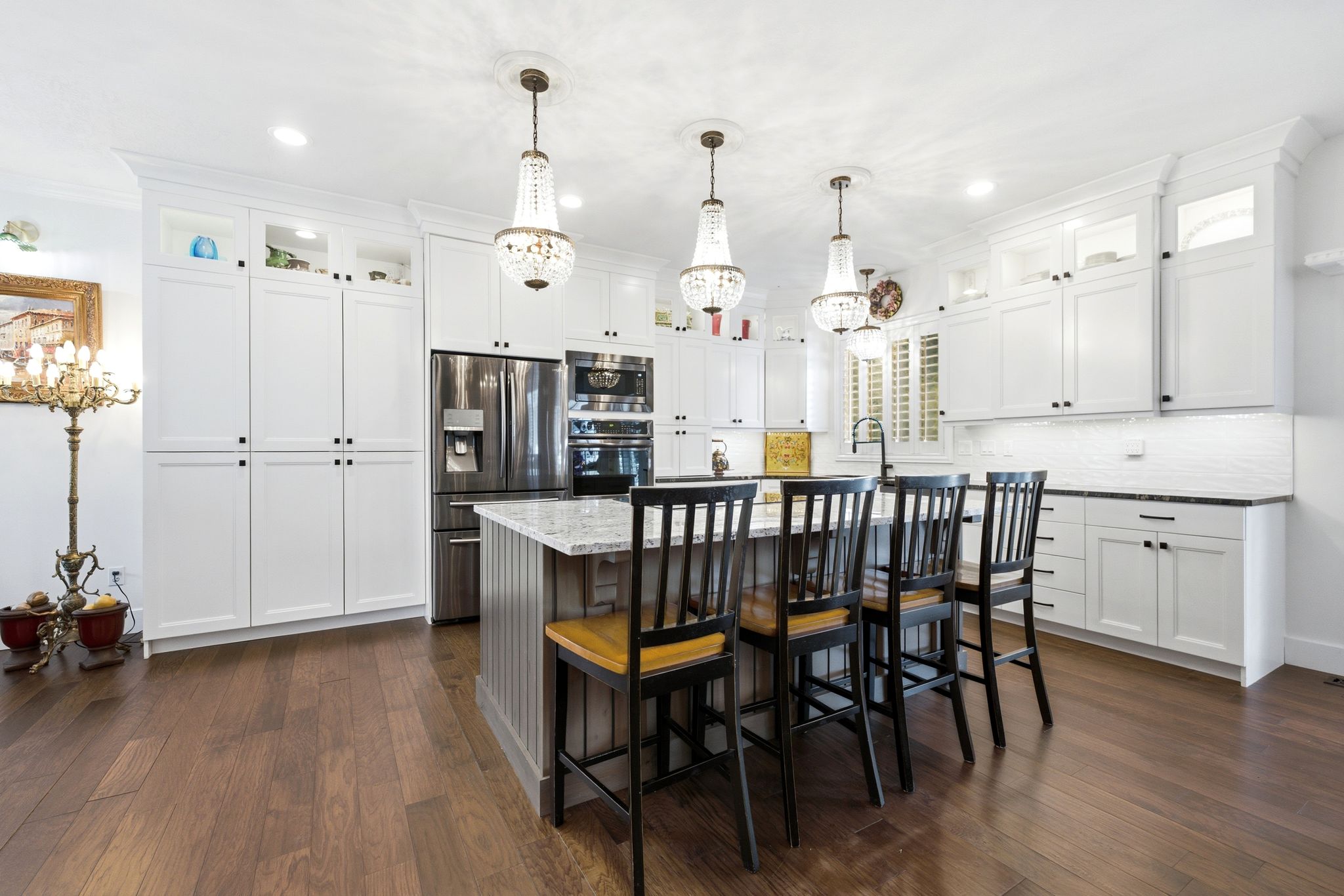Bright kitchen featuring white shaker cabinetry, stainless steel appliances, a large center island with seating, pendant lighting, and wood-finish flooring