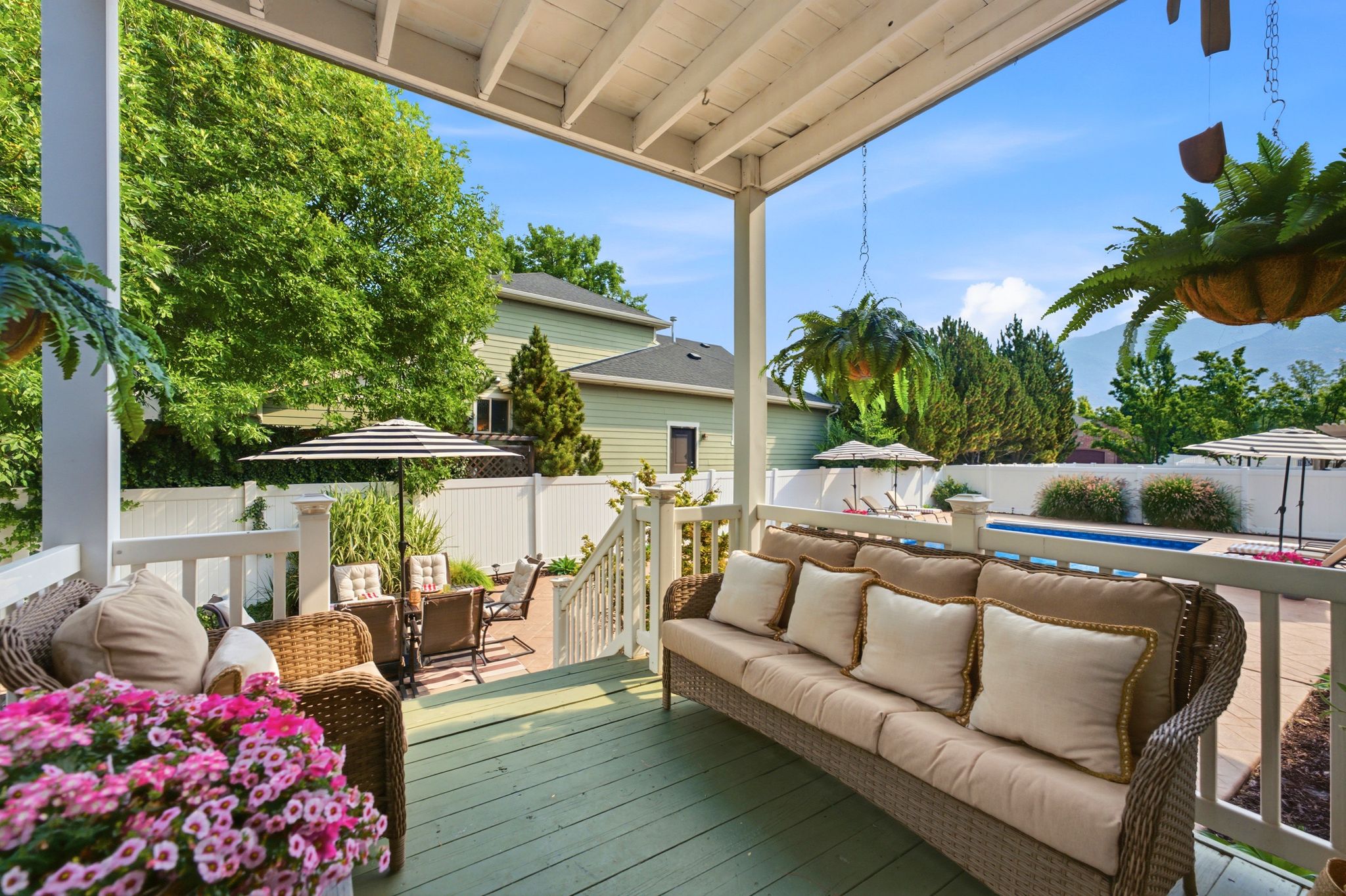 Covered porch with painted wood flooring, white railings, and a direct line of sight to a patio area and an in-ground swimming pool