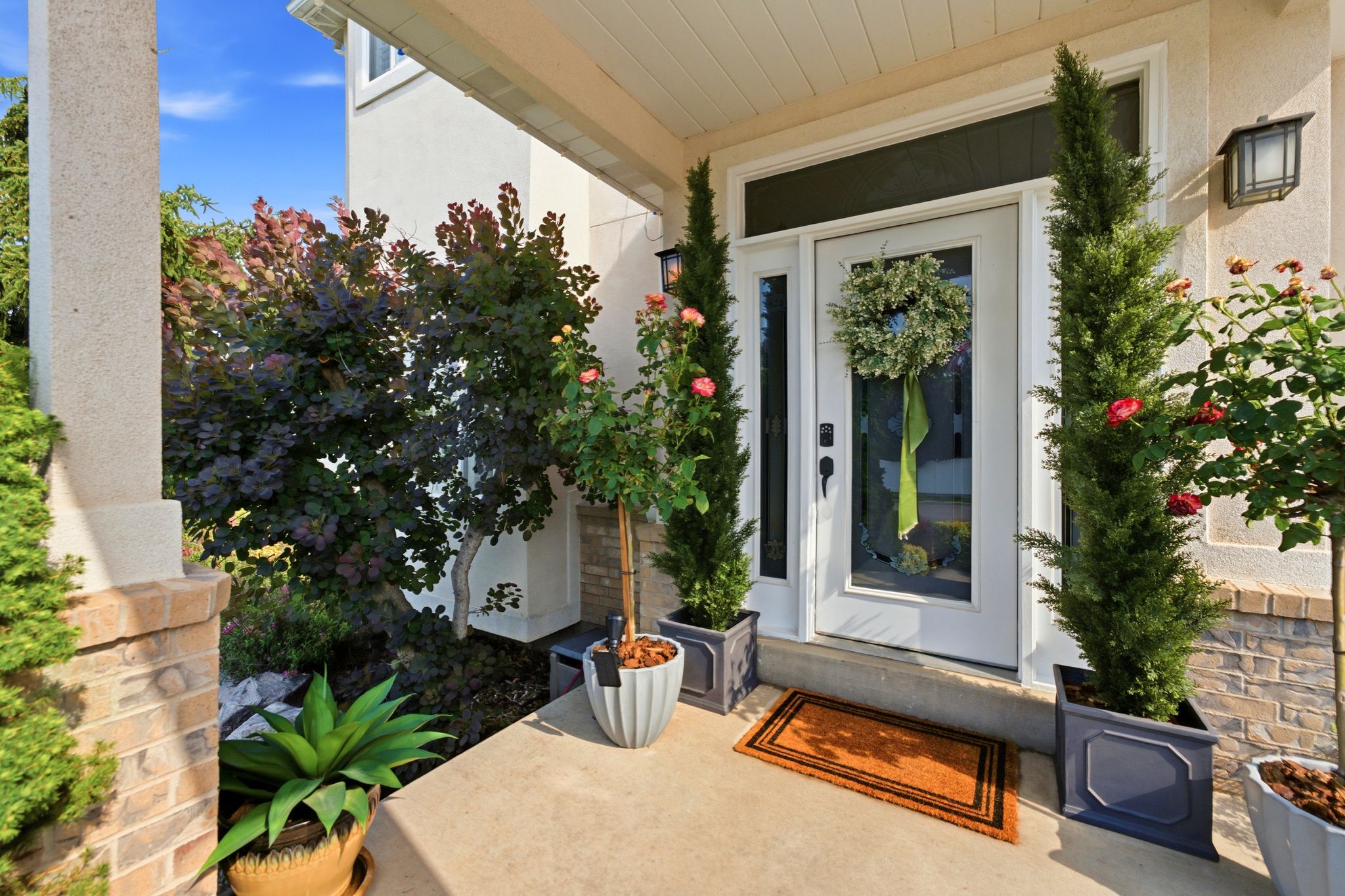 Covered entry with concrete flooring, framed by mature plantings and a textured stucco exterior