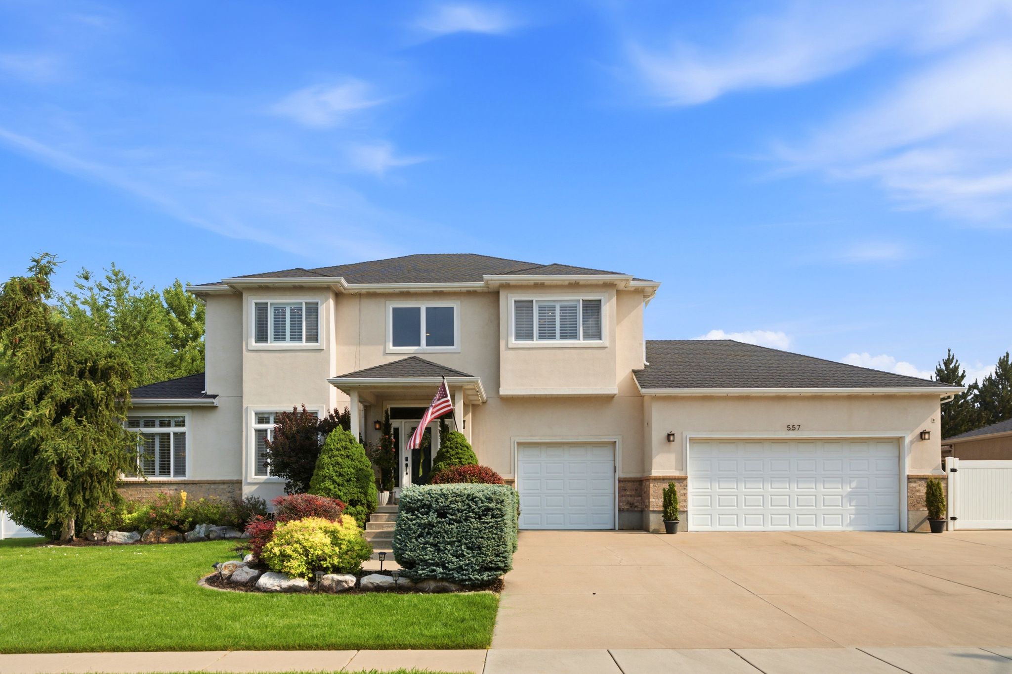 Stucco exterior residence featuring a covered entry, established landscaping, dual garage doors, and a concrete driveway
