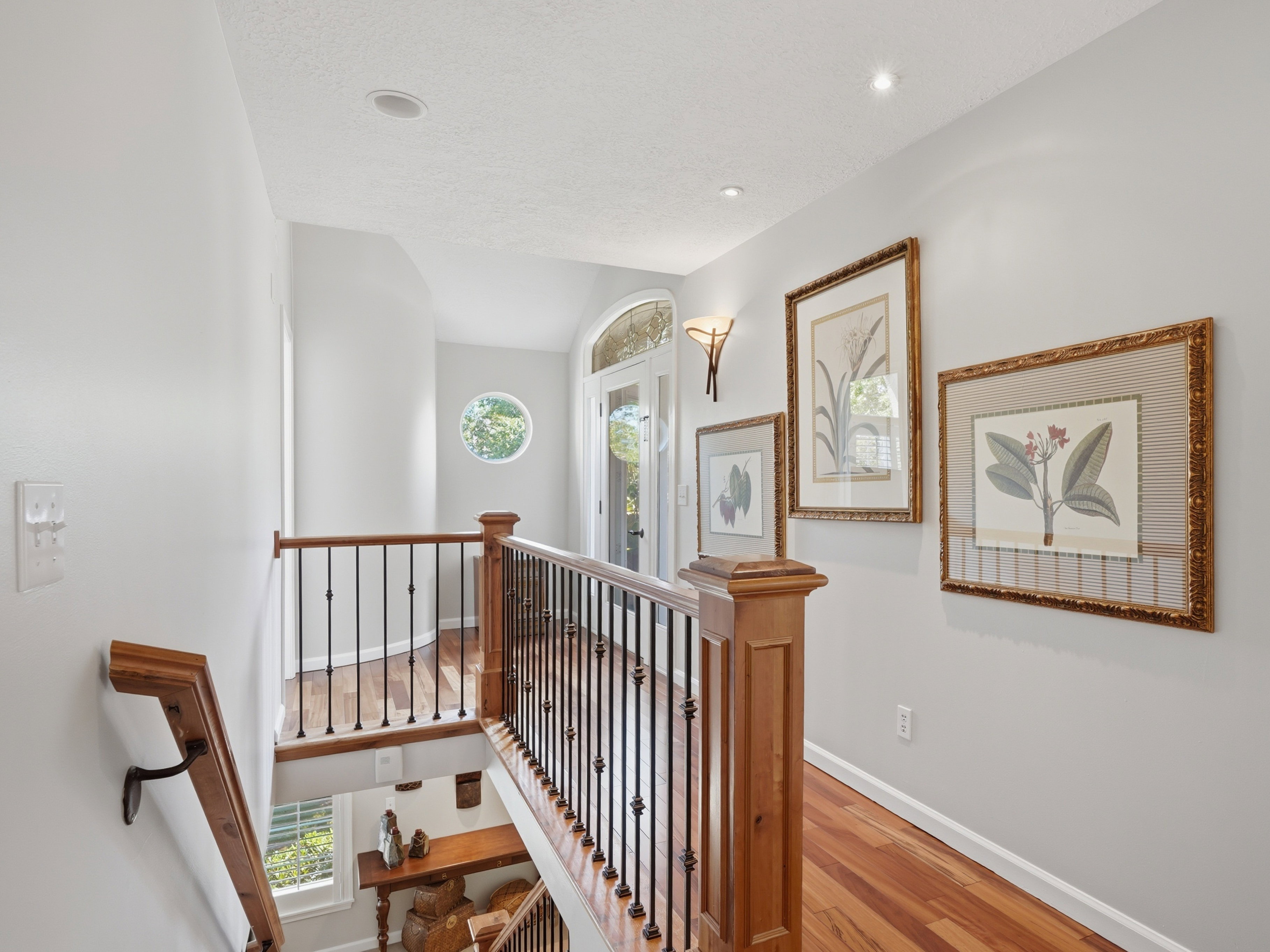 Wood flooring throughout the hallway and landing, complemented by a wood and wrought iron staircase railing