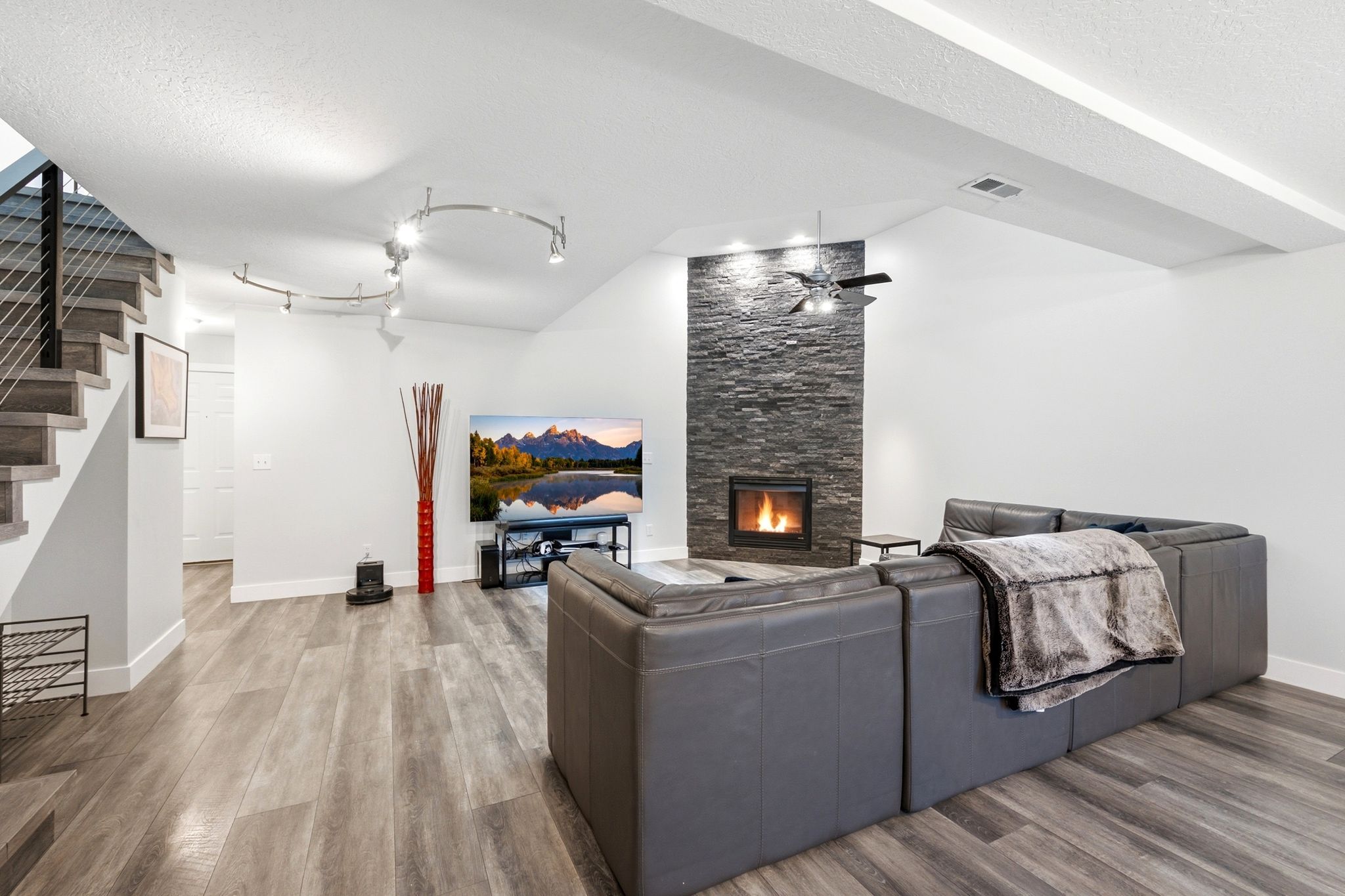 Living area featuring a floor-to-ceiling stacked stone fireplace with an inset firebox, wood-finish flooring, and a contemporary staircase with metal cable railings
