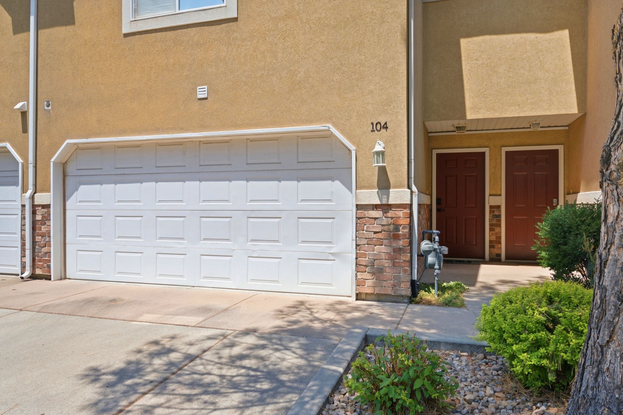 Stucco exterior with brick veneer accents, featuring a paneled garage door and two paneled entry doors