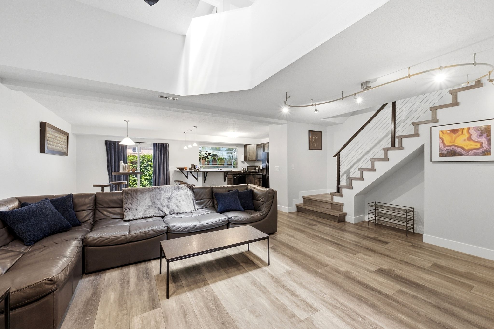 Spacious lower level featuring wood-finish flooring, a modern open-tread staircase with cable railing, track lighting, and recessed ceiling lights