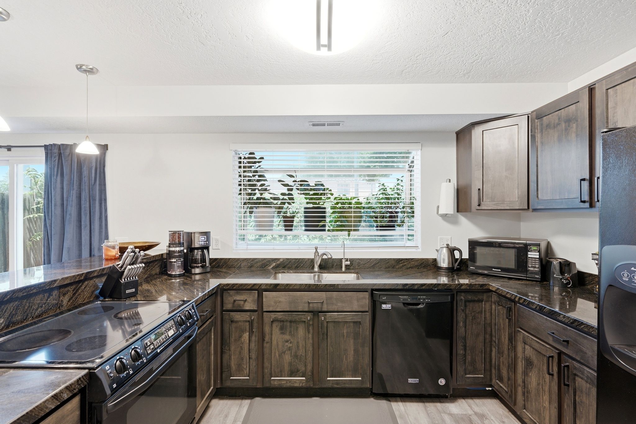U-shaped kitchen featuring wood-finish cabinetry, dark countertops, and black appliances including a dishwasher and range