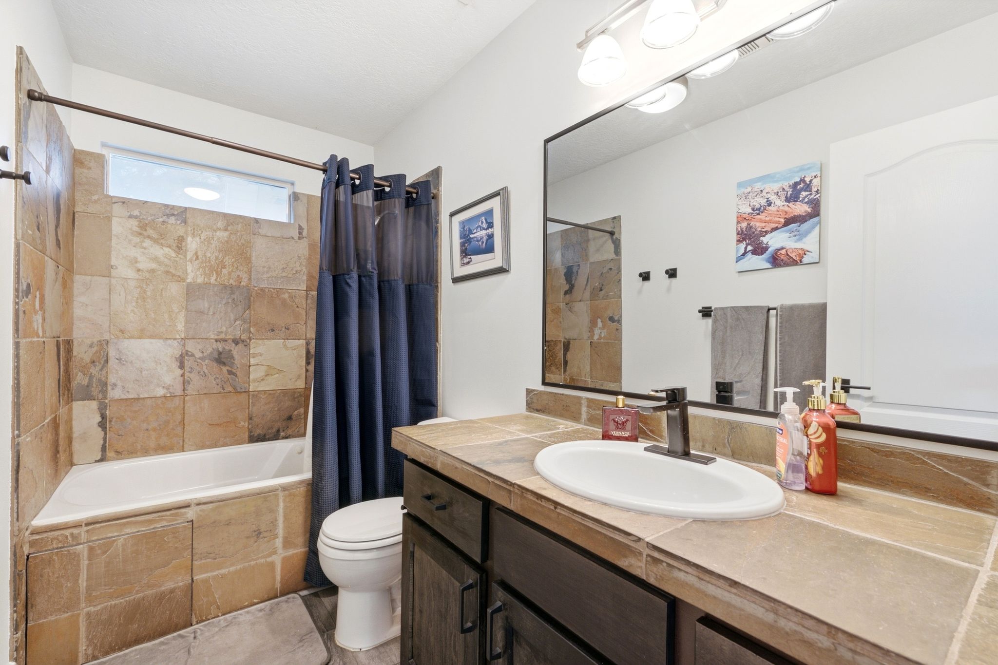 Bathroom featuring a tiled shower surround, built-in bathtub, window, dark wood-finish vanity with an integrated sink, and an expansive vanity mirror