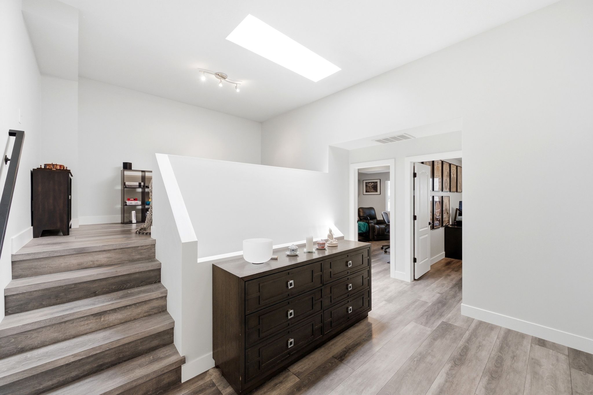Upper landing featuring a skylight, light wood-finish flooring, white walls, and a modern track light fixture
