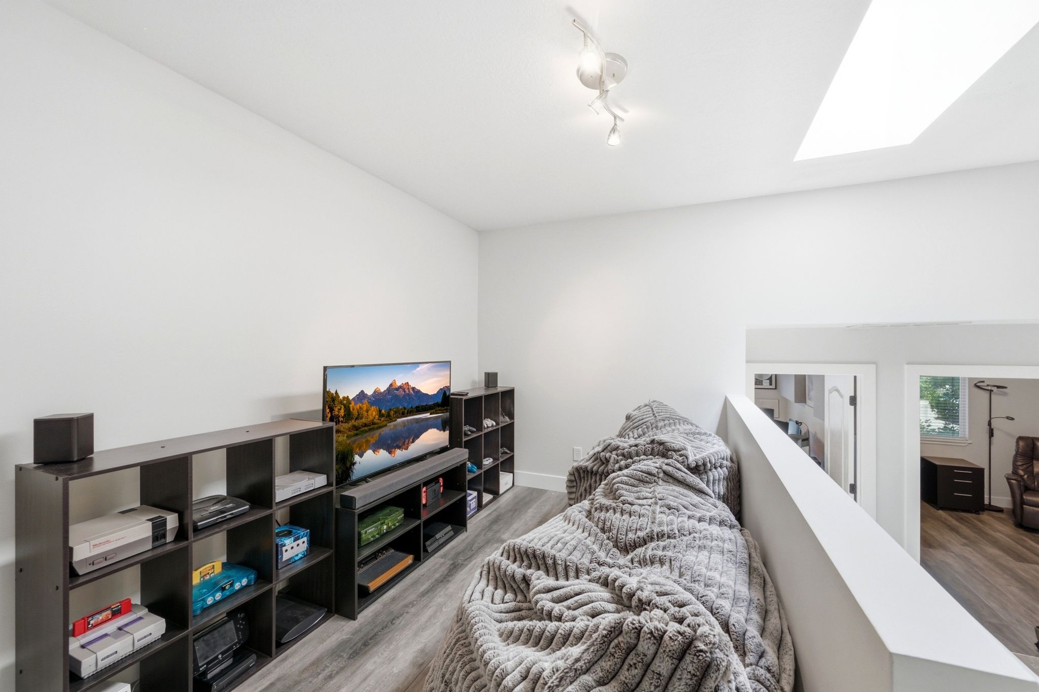 Loft area featuring light wood-finish flooring, a white ceiling with a skylight, and track lighting