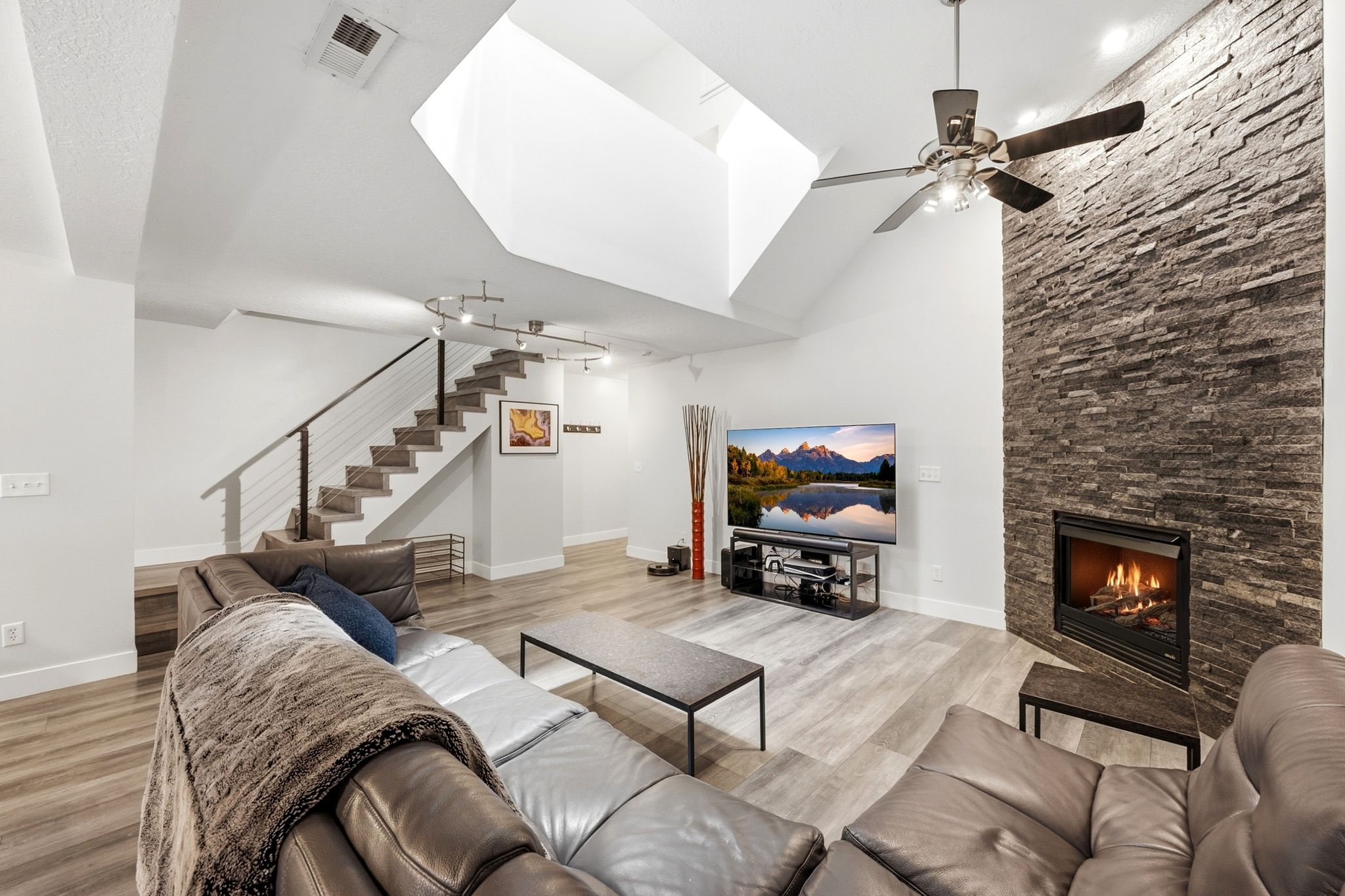 Spacious living area featuring a stacked stone fireplace with a black surround, vaulted ceilings, and recessed lighting