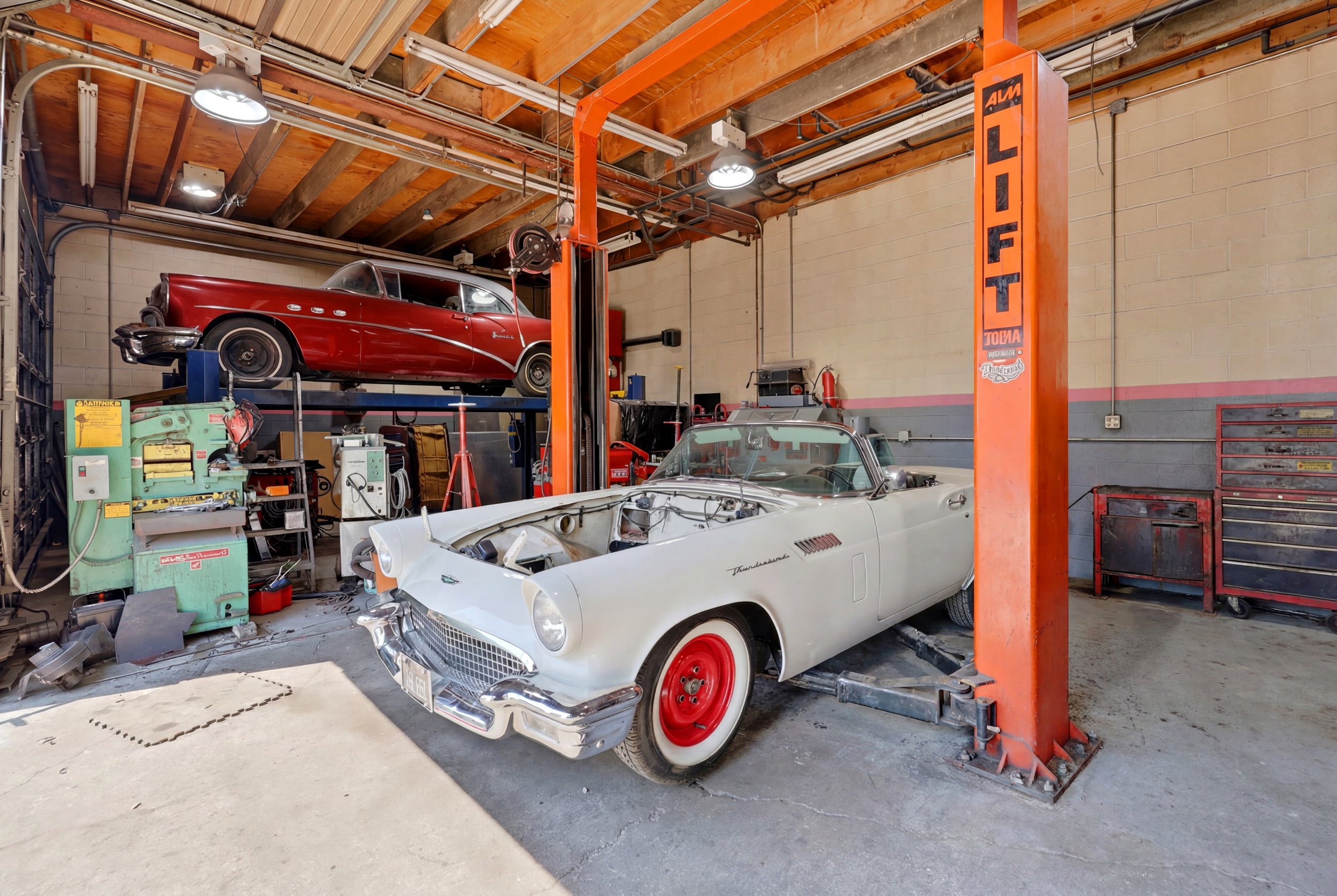 Spacious garage featuring a professional vehicle lift, exposed wood beam ceiling, concrete flooring, and built-in storage solutions