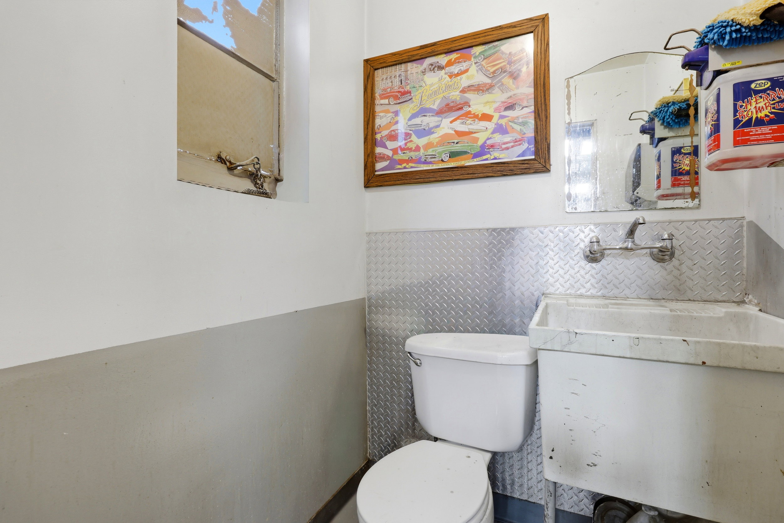 Utility room featuring a white toilet, wall-mounted utility sink, and diamond plate wainscoting