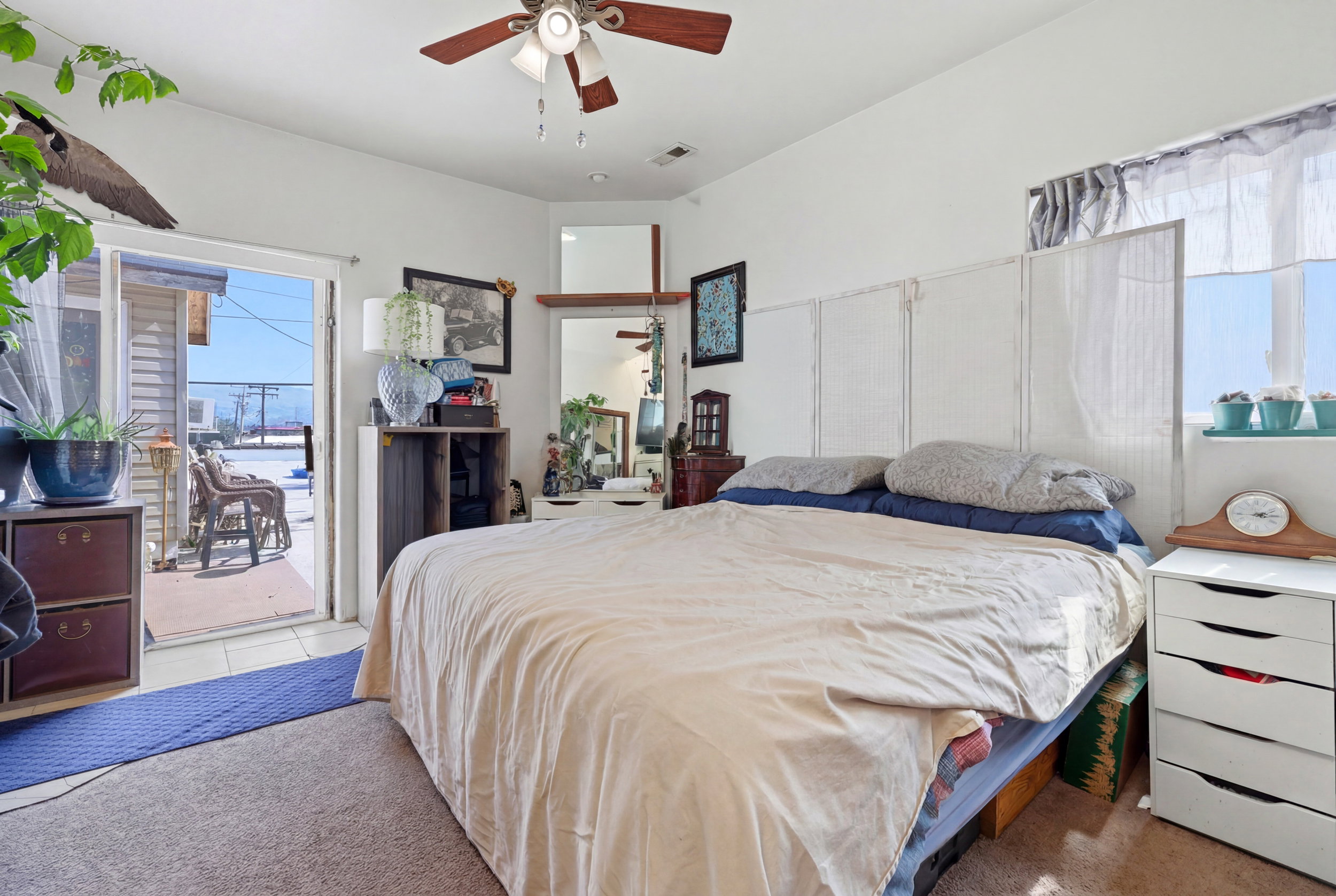 Carpeted interior space featuring a ceiling fan with integrated lighting, a corner vanity with a mirror, and a window with a sheer curtain