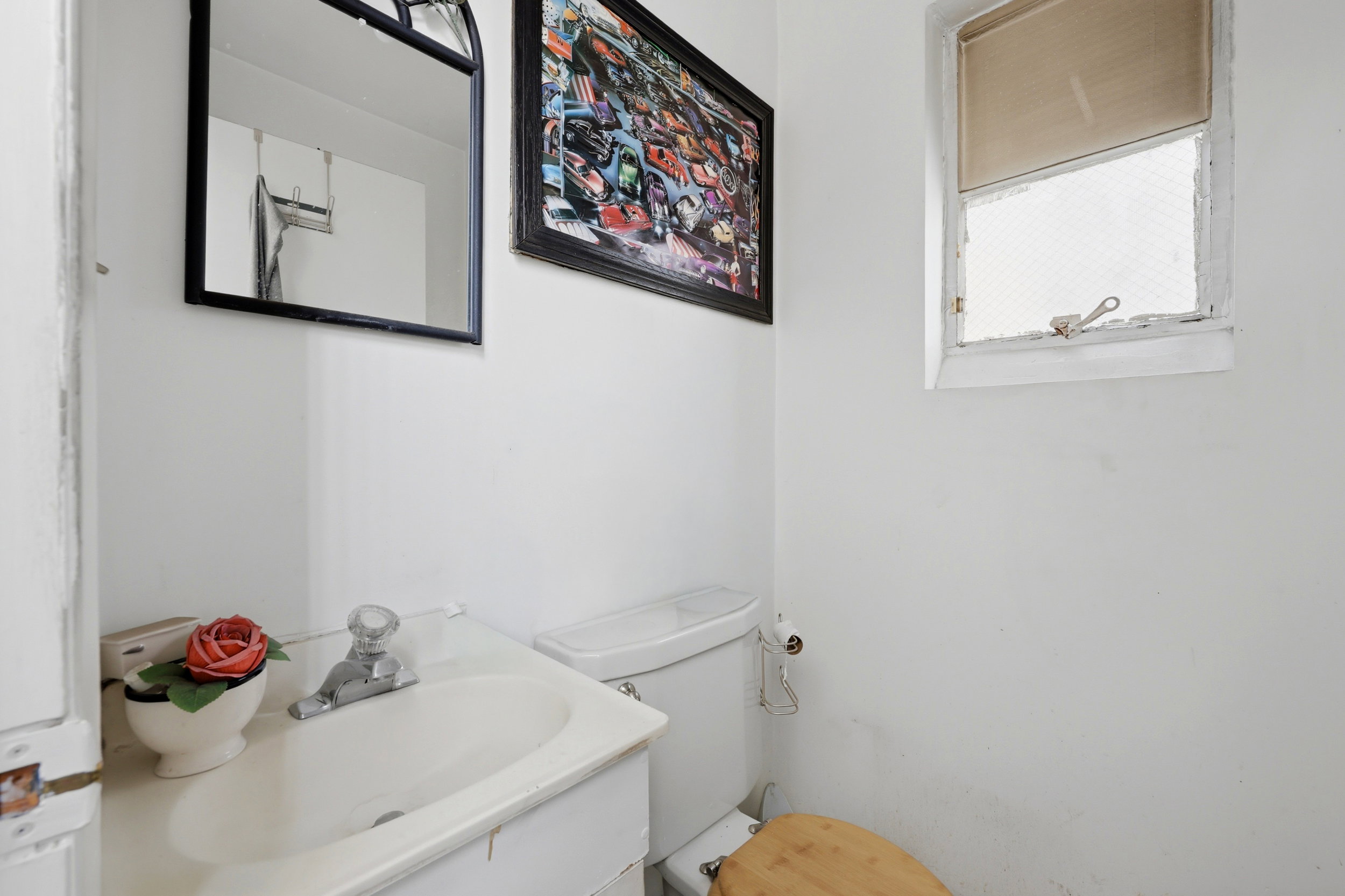 White bathroom featuring a vanity with integrated sink, a toilet, a small window, and a wall-mounted mirror