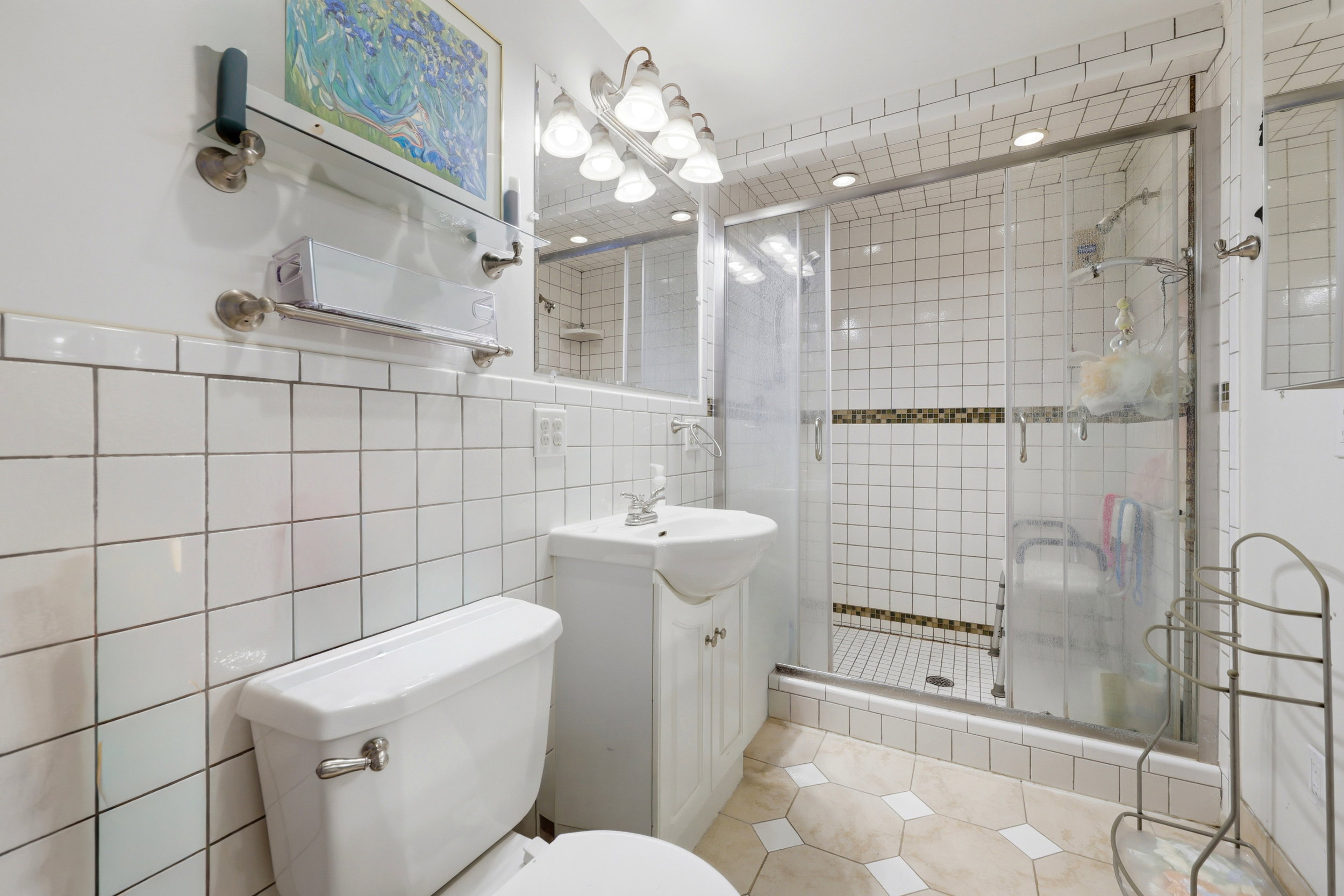 Tiled bathroom featuring a glass-enclosed shower with a mosaic accent band, a pedestal sink with vanity storage, and a built-in medicine cabinet