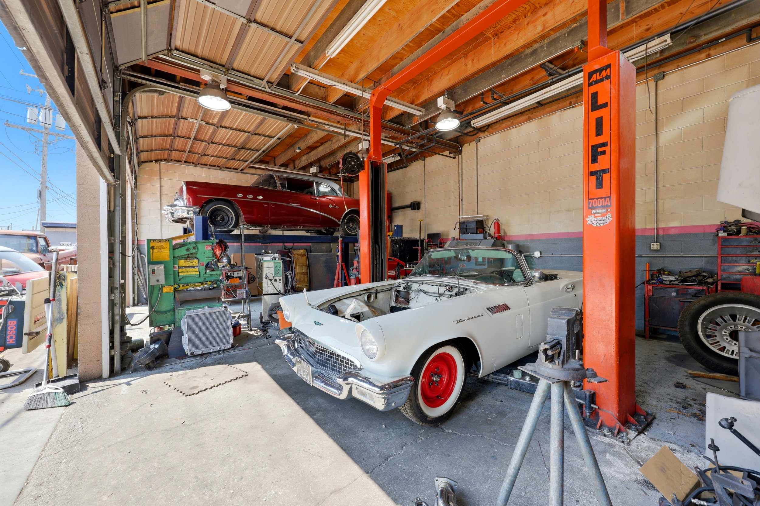Industrial garage space featuring a roll-up door, exposed wood ceiling beams, concrete flooring, and an installed vehicle lift system
