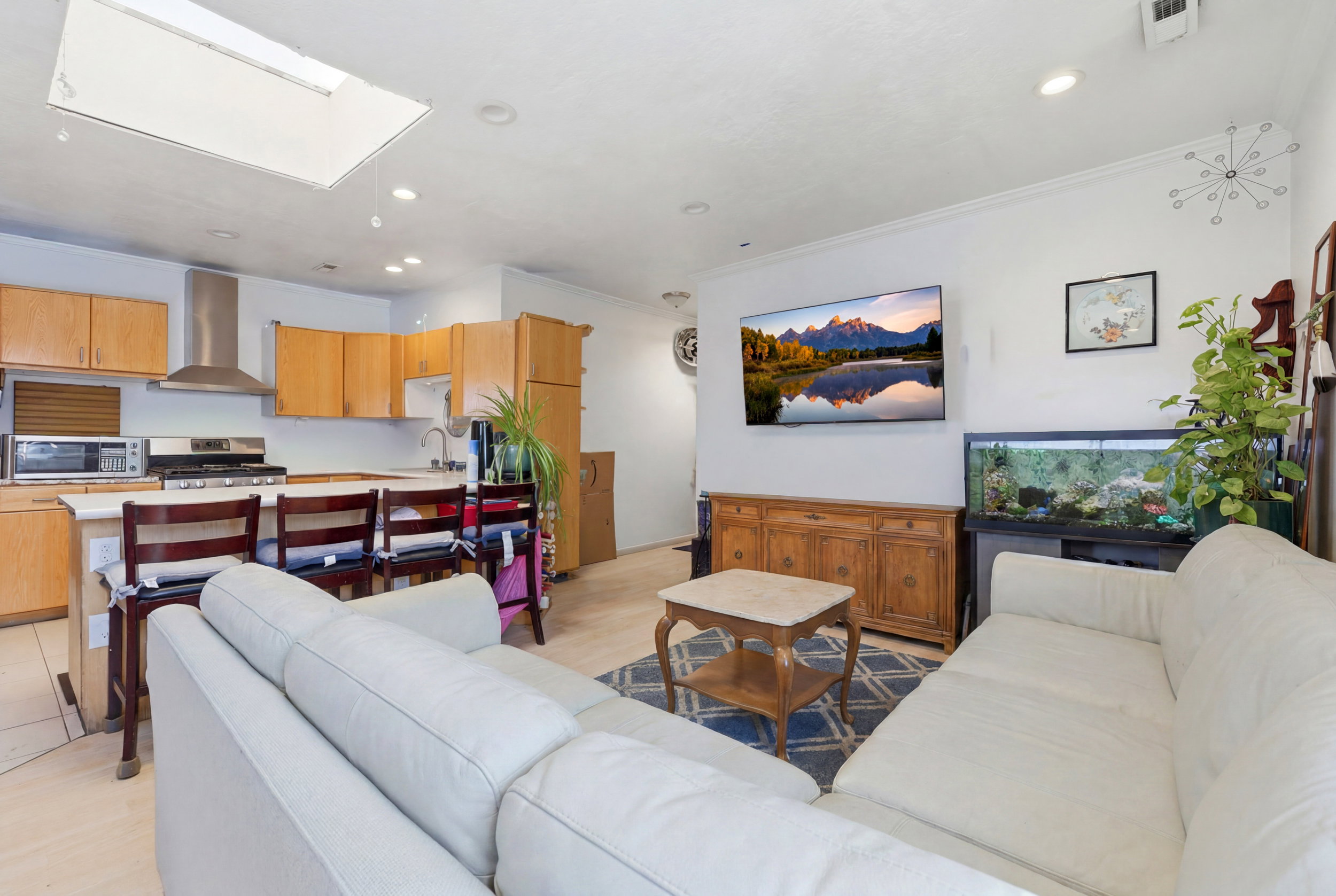 Open-concept living space featuring a kitchen with light wood cabinetry, white countertops, and stainless steel appliances