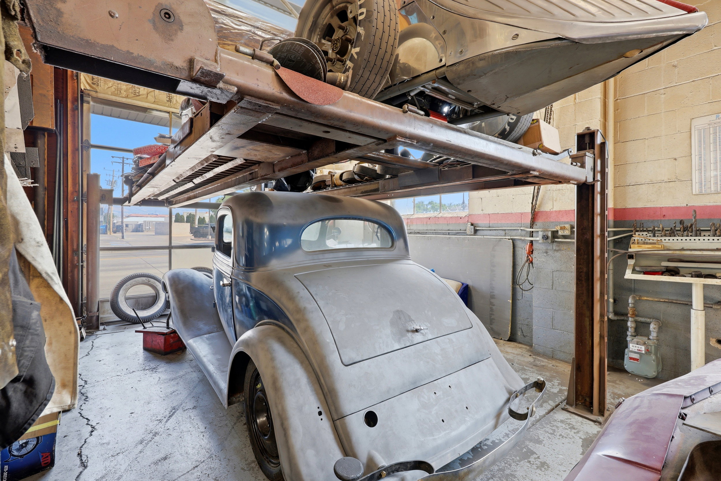 Automotive service bay featuring a hydraulic lift system, concrete flooring, exterior-facing windows, and block wall construction
