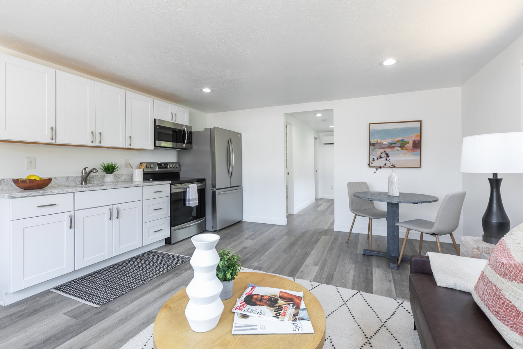 Modern kitchen featuring white cabinetry, stone countertops, stainless steel appliances, and wood-finish flooring