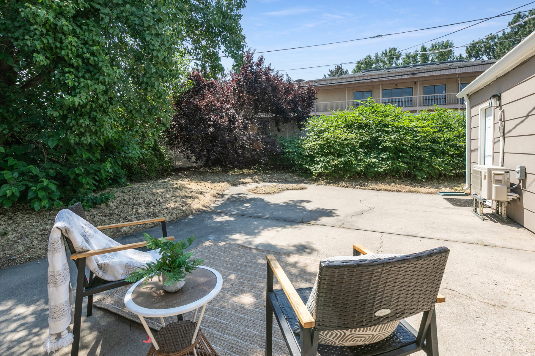 Paved patio area featuring lush perimeter landscaping and a building exterior with horizontal siding
