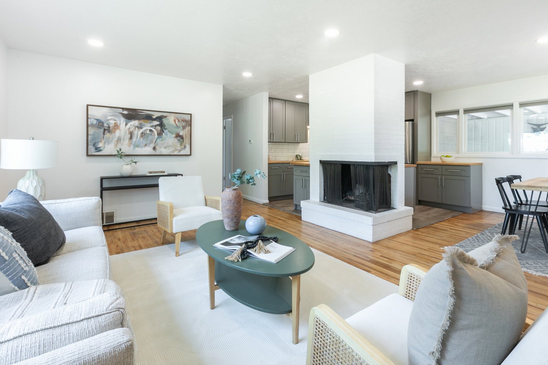 Open-concept living space featuring wood-finish flooring, a white brick fireplace, recessed lighting, and a kitchen with gray cabinetry and light wood-finish countertops
