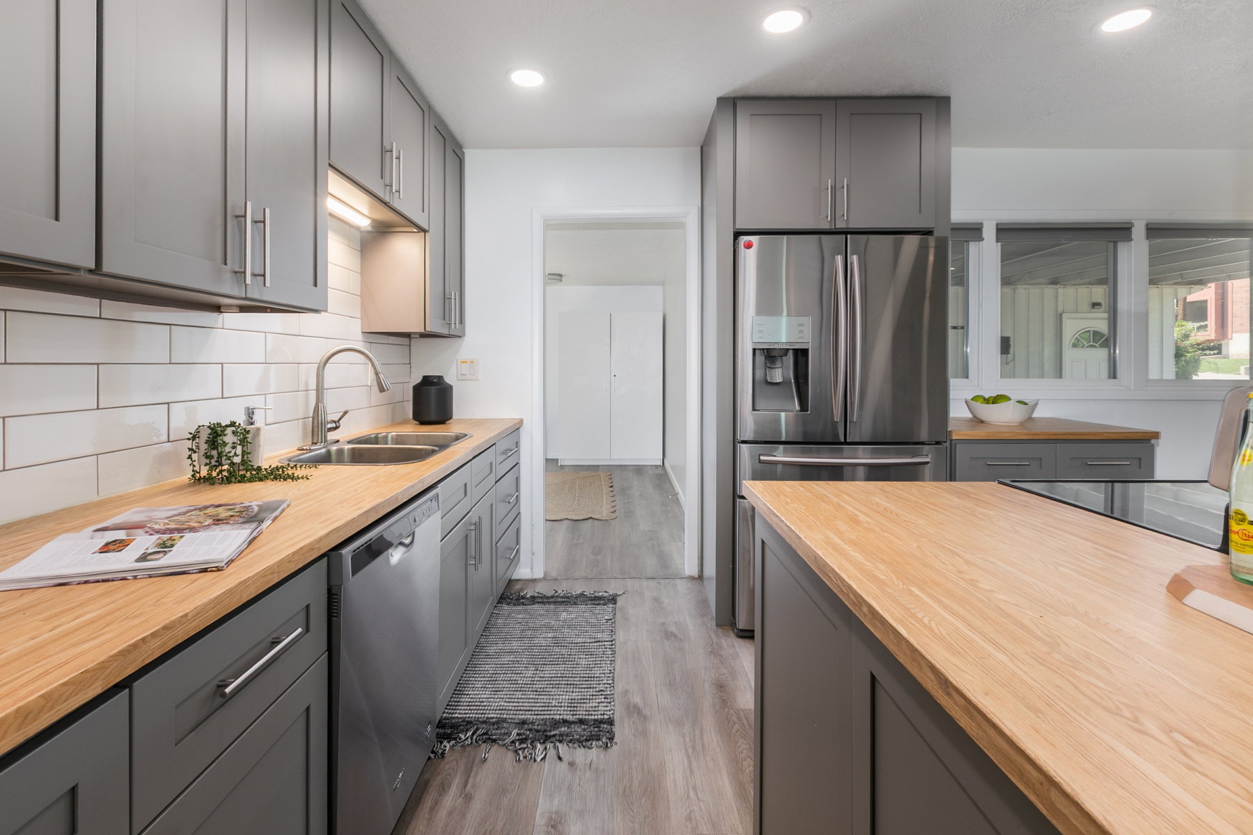 Contemporary kitchen featuring wood-finish countertops, subway tile backsplash, stainless steel appliances, and gray cabinetry with brushed nickel hardware