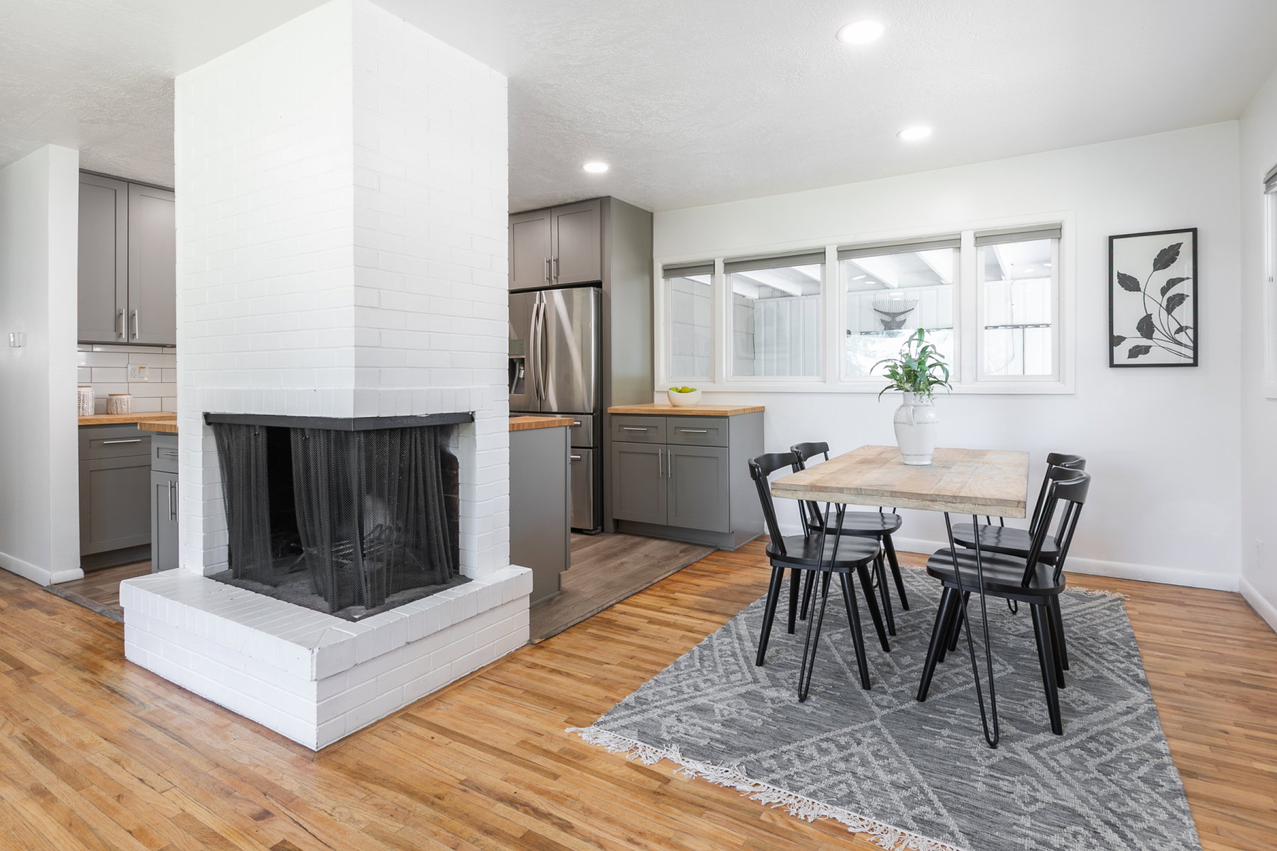 Central white brick fireplace with a black mesh screen, hardwood flooring, recessed lighting, and multiple windows providing natural light