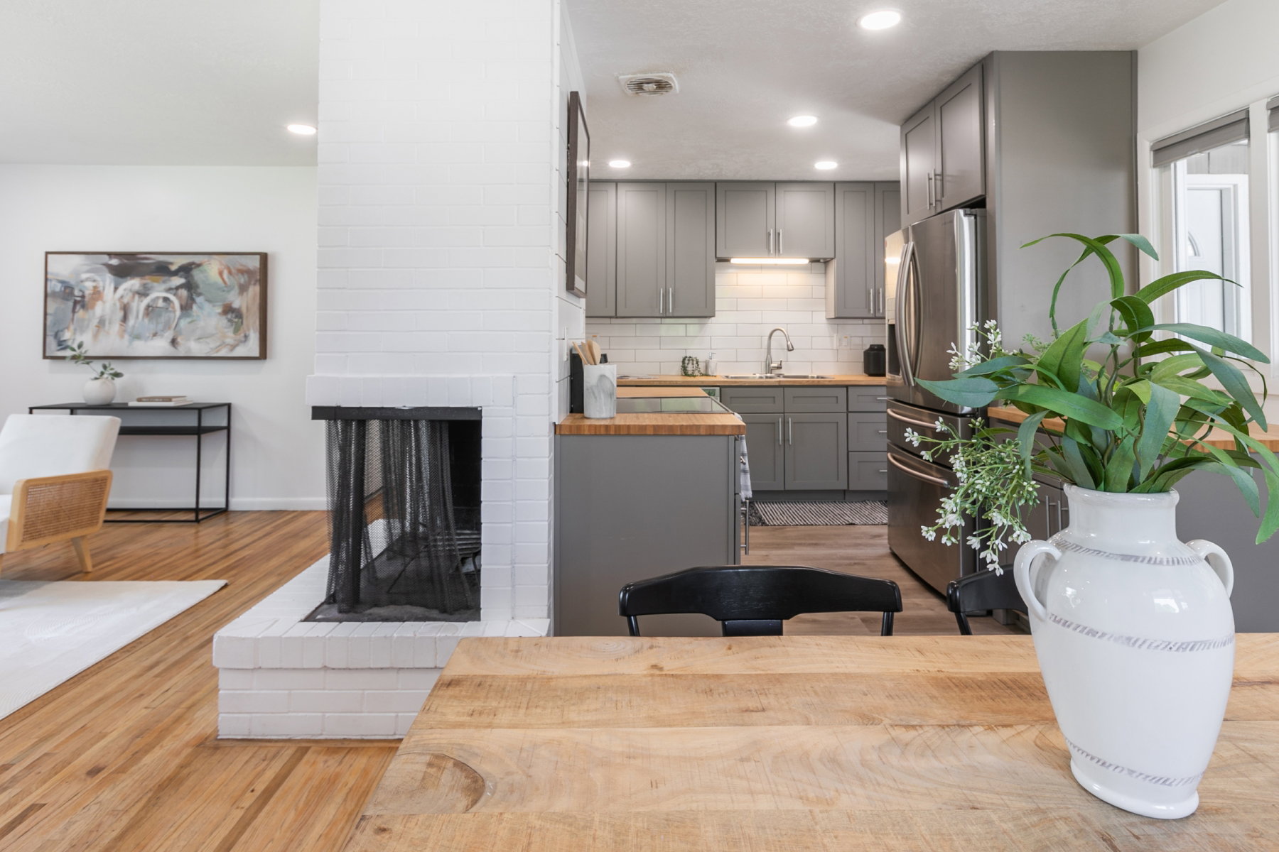 Open-concept living space featuring wood-finish flooring, a white brick fireplace, grey cabinetry, stainless steel appliances, and butcher block countertops