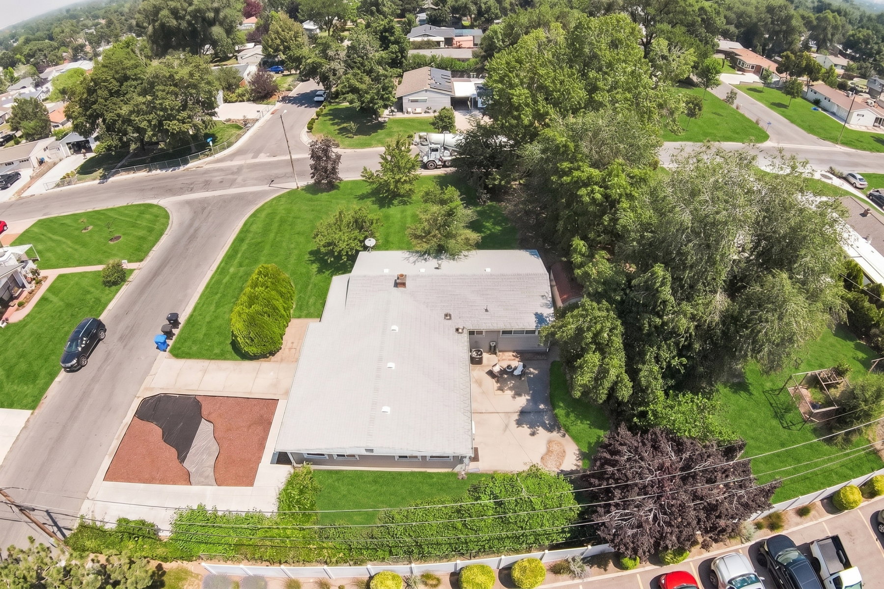 Expansive corner lot featuring a residential structure with a light-colored roof, a concrete driveway with a decorative gravel inlay, mature trees, and a substantial grassy area