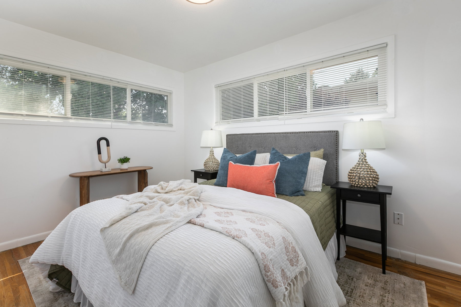 Bright bedroom featuring multiple windows with blinds, wood-finish flooring, and a flush-mount ceiling light