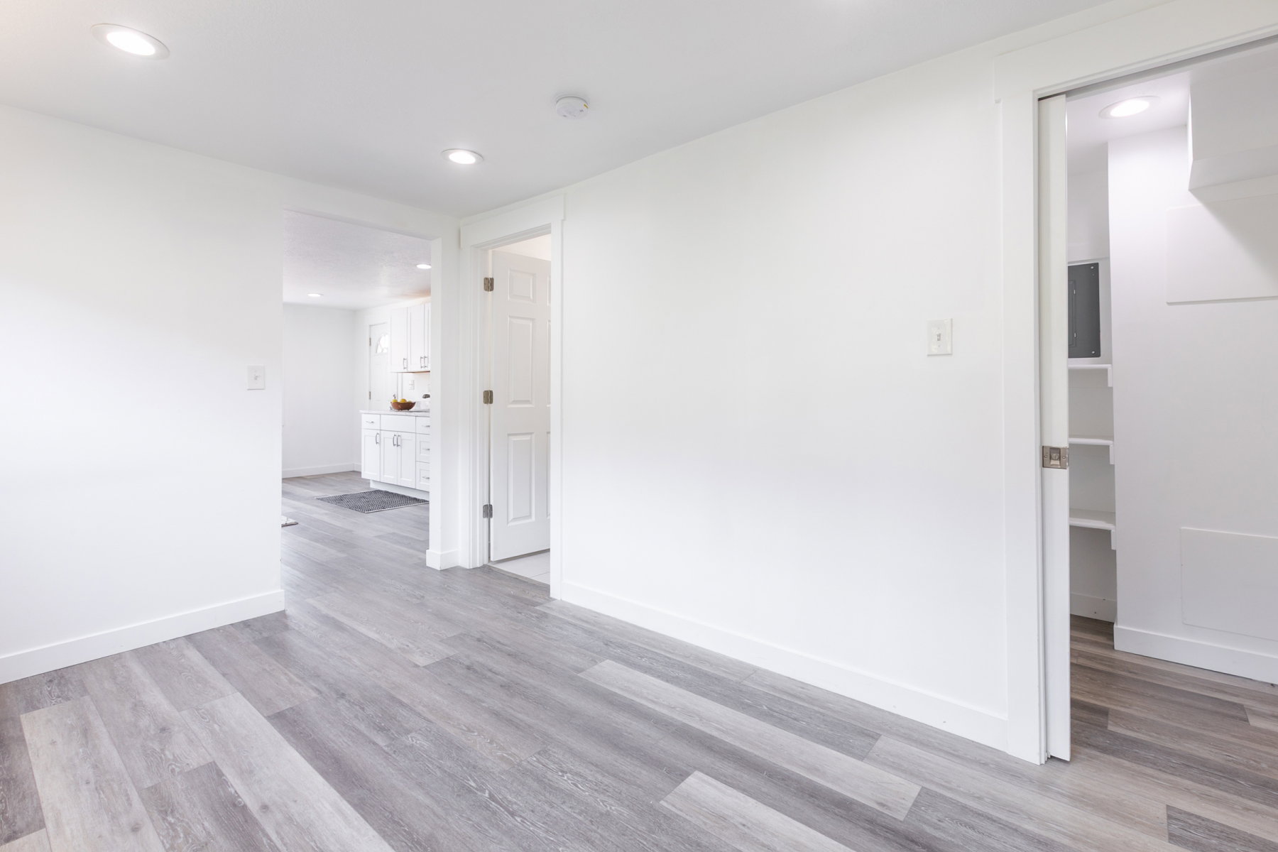 Spacious interior room featuring light gray wood-finish flooring, white walls, recessed ceiling lights, and white trim