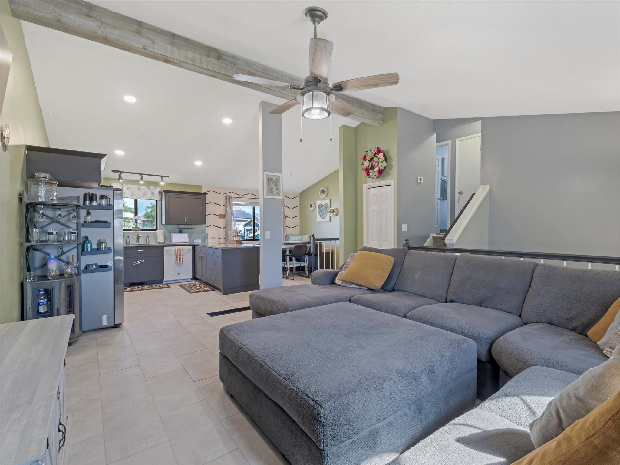Open-concept living space featuring vaulted ceilings with a decorative wood beam, recessed lighting, and tile flooring