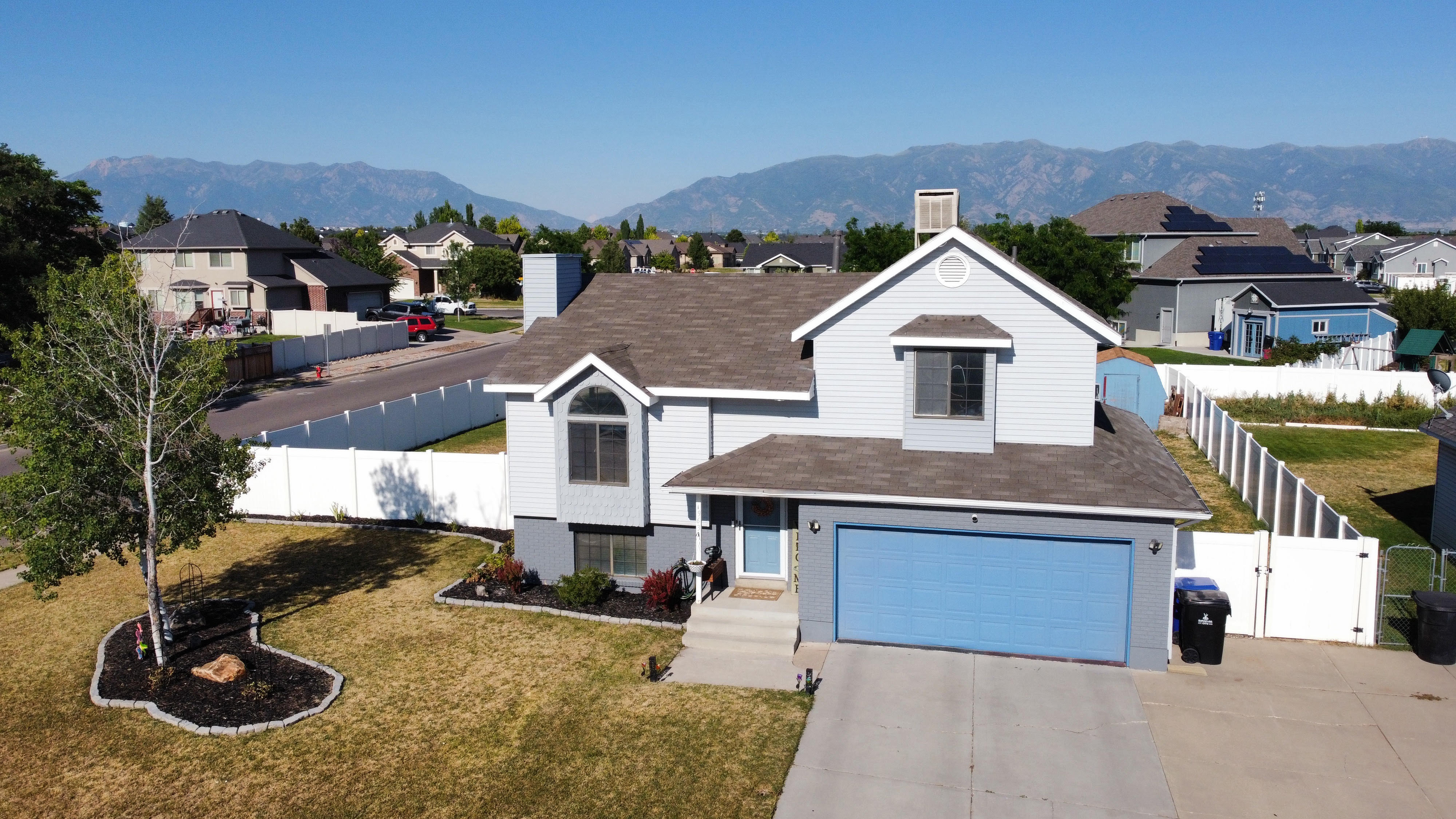 Two-story residence featuring light blue siding with gray accent trim, a two-car garage with a blue door, and a front yard with a mature tree