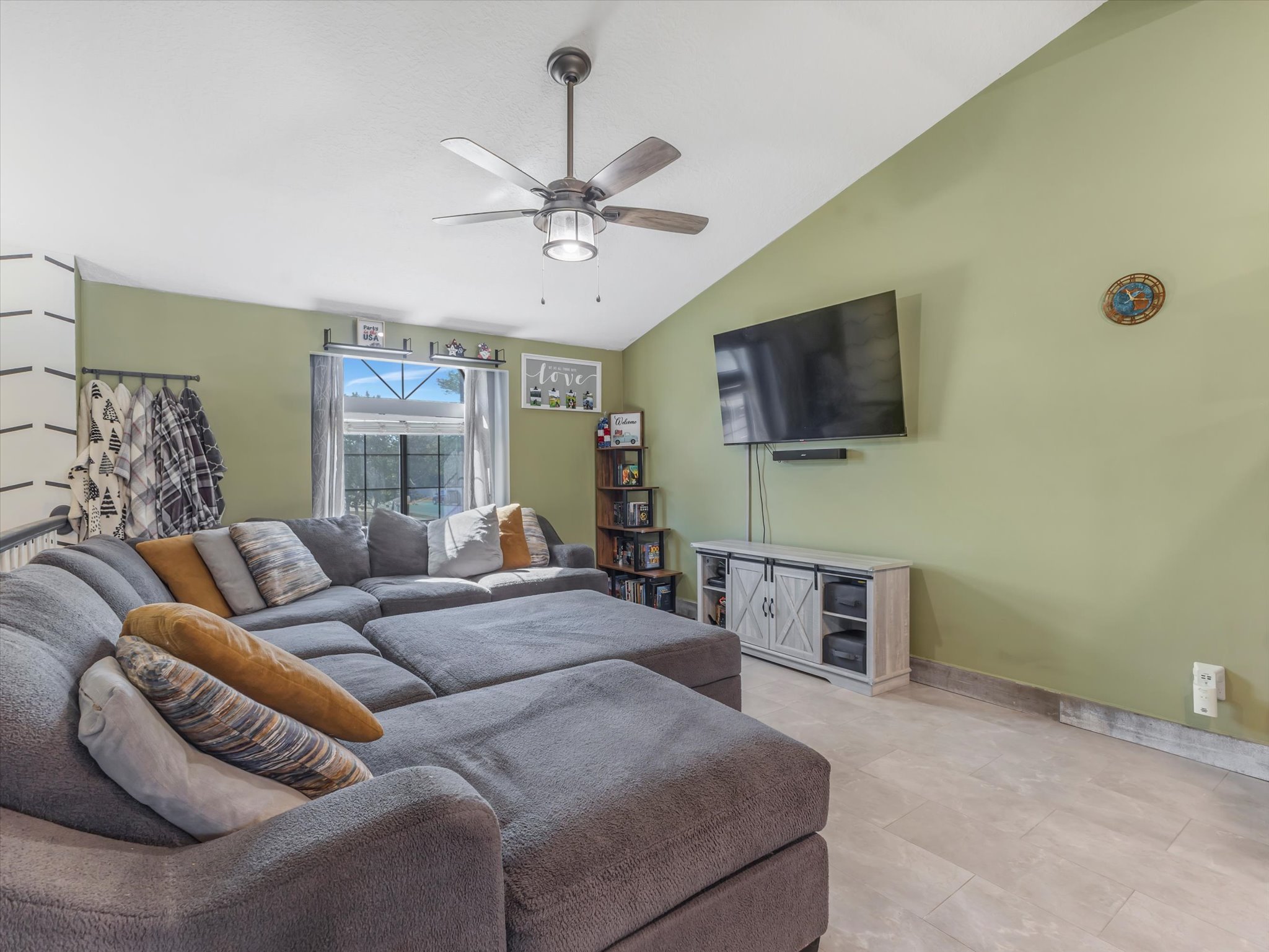 Living area featuring vaulted ceilings, a ceiling fan with integrated lighting, and tile flooring
