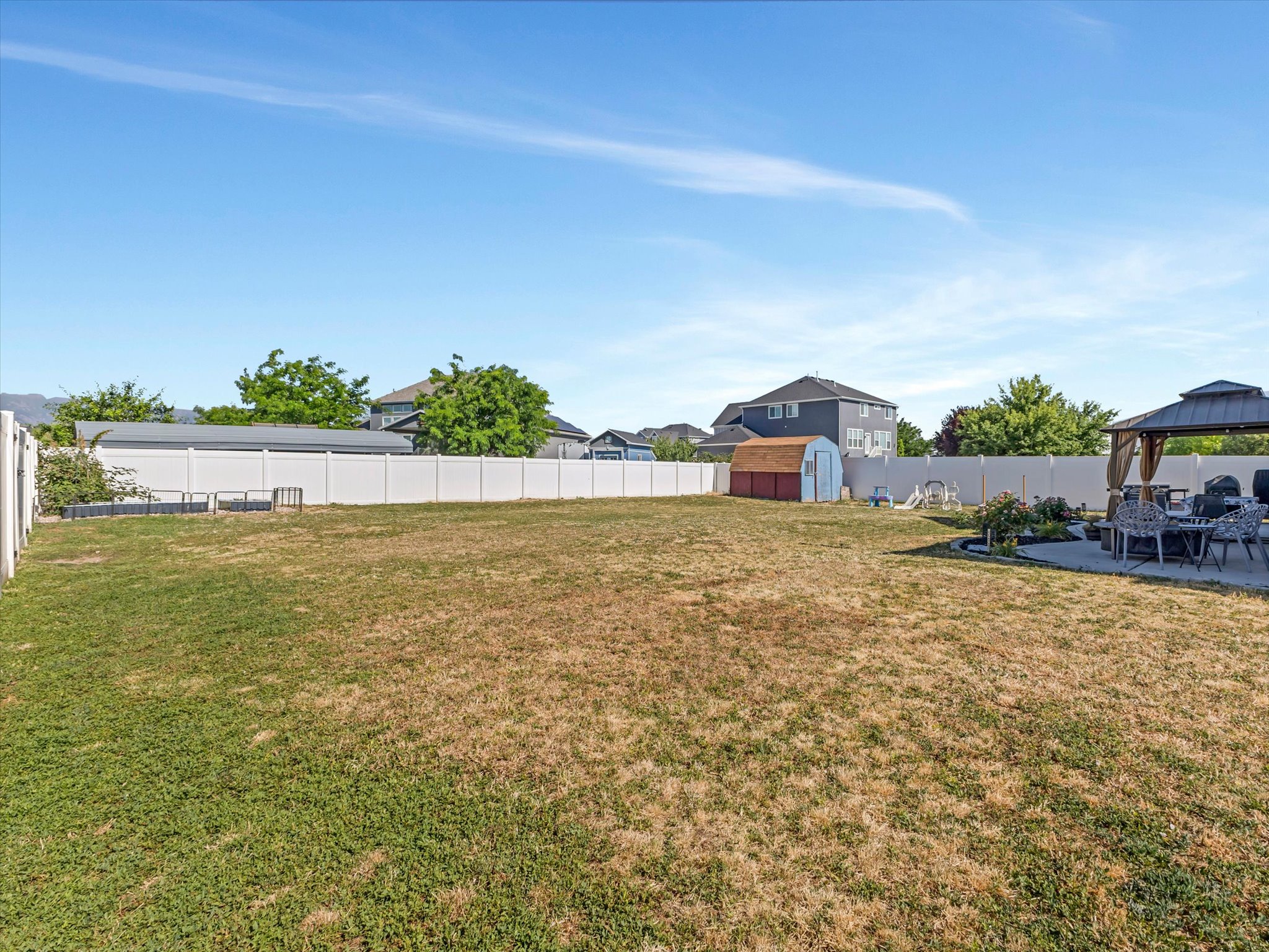 Expansive backyard featuring a white privacy fence, a concrete patio, and a covered gazebo